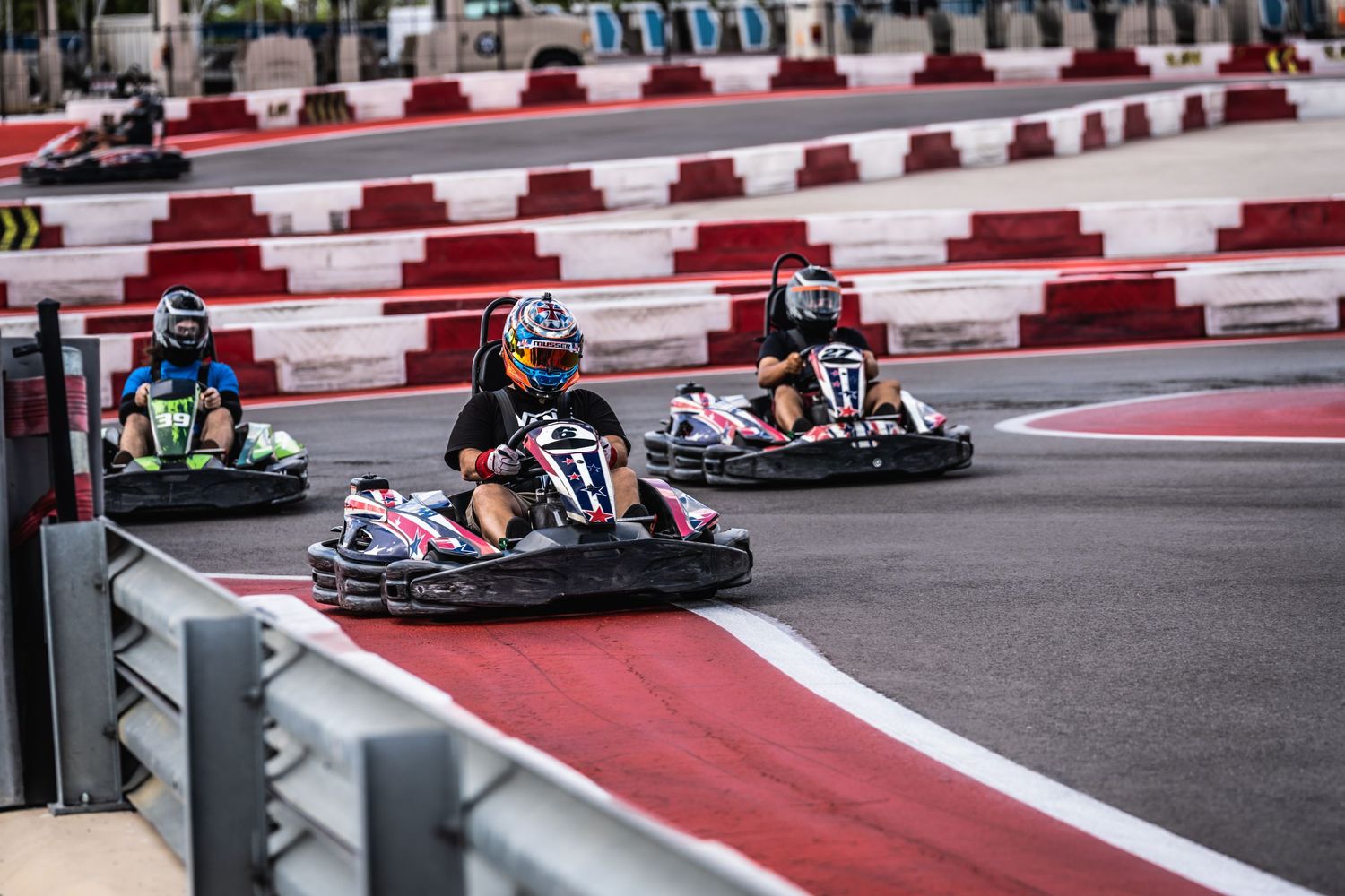 Several go-karts competing on a race track with red and white barriers.