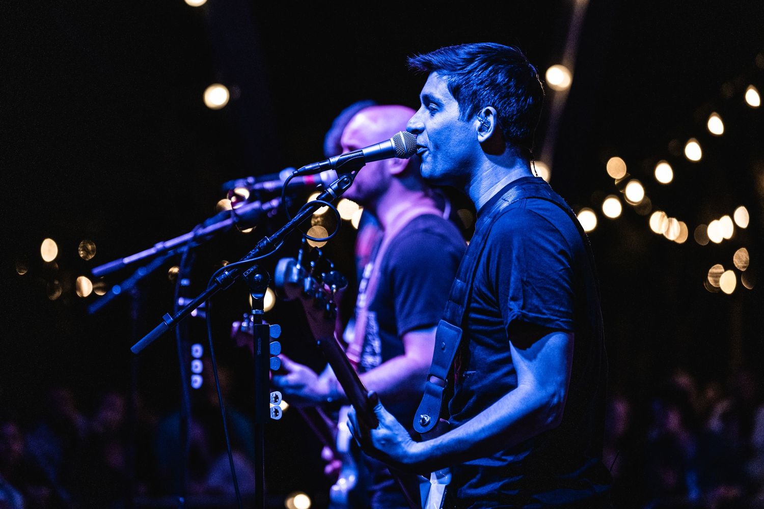 Band performs on dark stage with string lights creating ambient atmosphere.