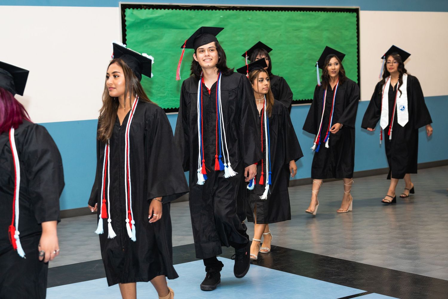 Graduates in black caps and gowns walking across stage during commencement ceremony.