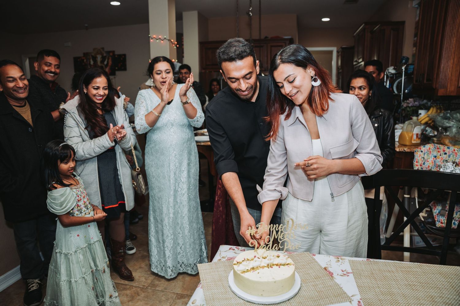 A joyful celebration as a couple cuts their white cake together while guests watch and smile in the background.
