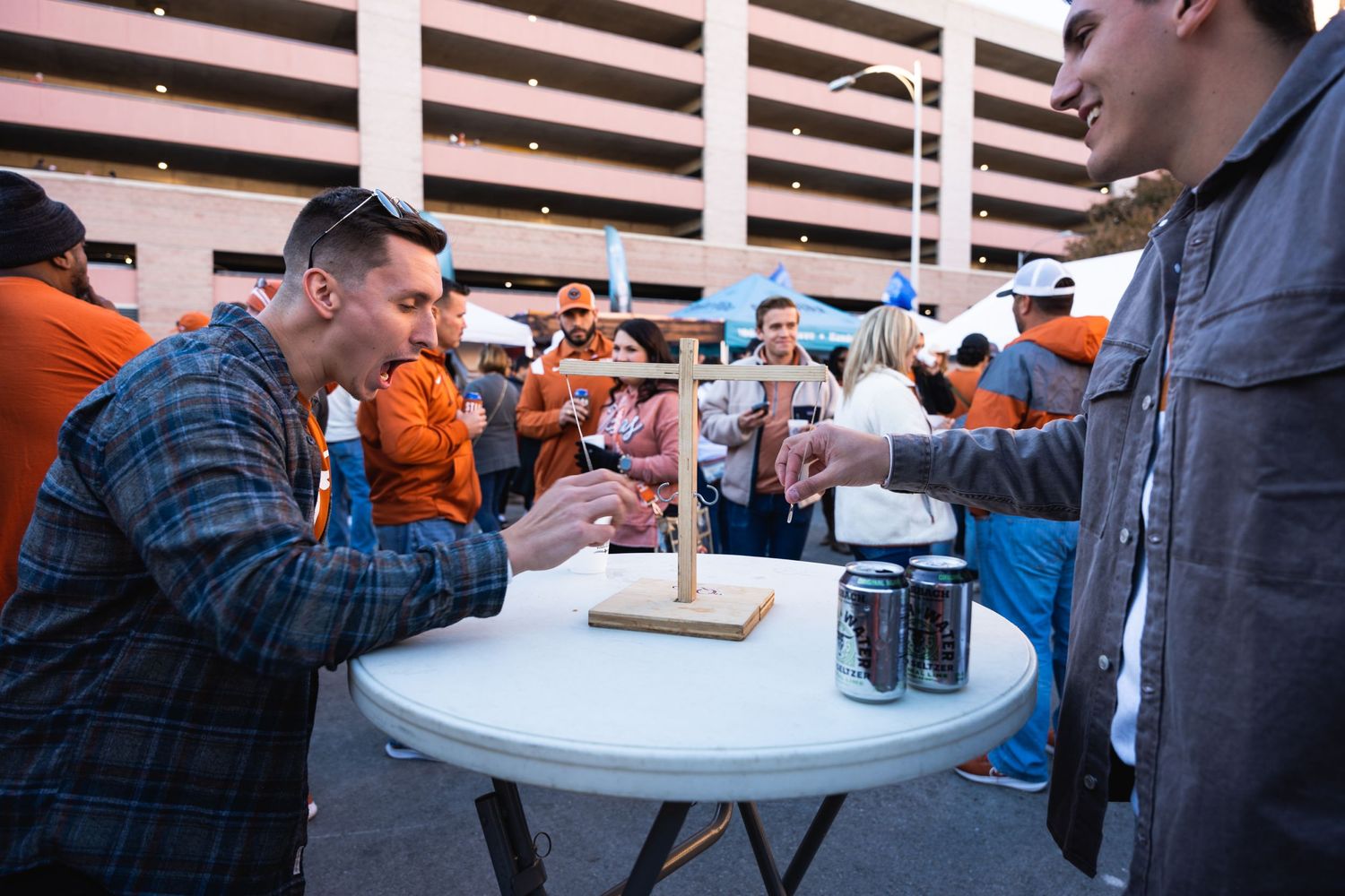 People gathered around a white table playing a drinking game at an outdoor event.