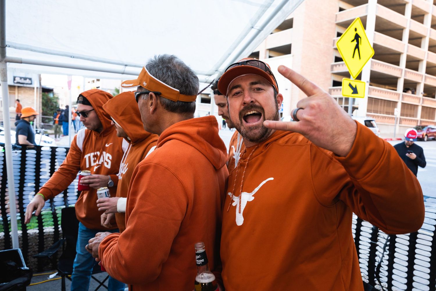 Excited sports fans wearing burnt orange university apparel celebrating together at a tailgate party.