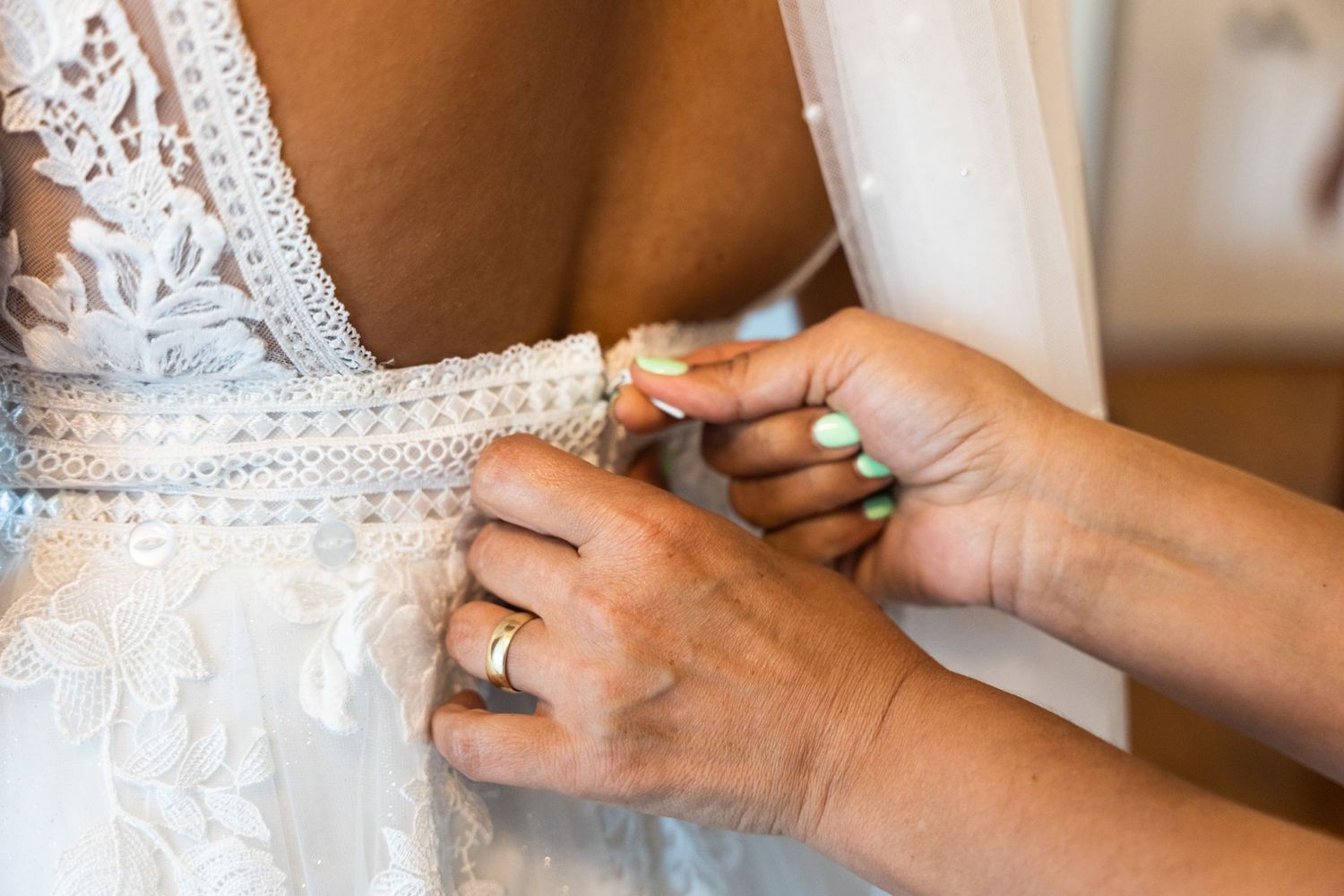 Close-up detail shot of hands buttoning an intricate lace wedding dress.