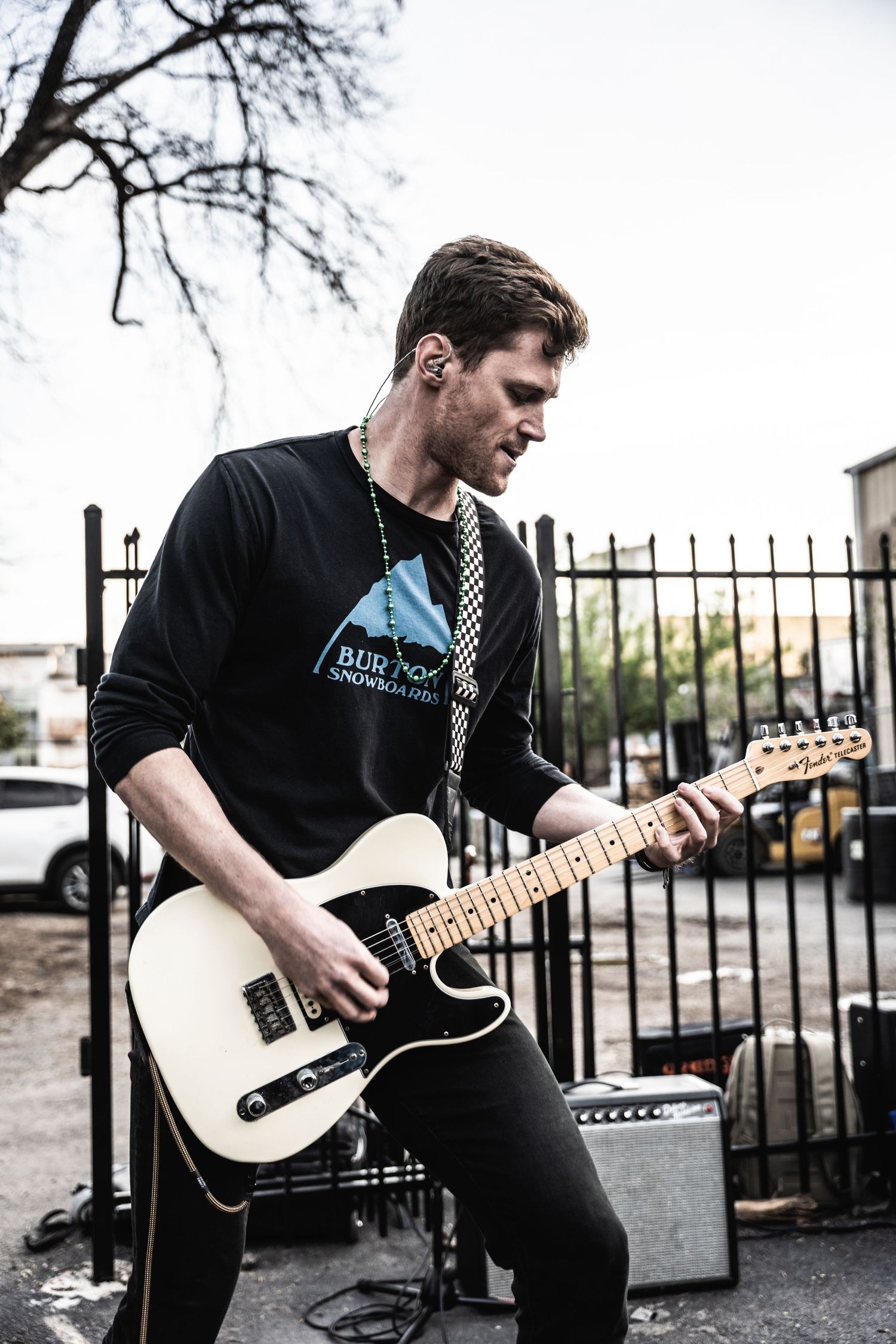 Guitarist performing with a white telecaster guitar against iron fence backdrop.