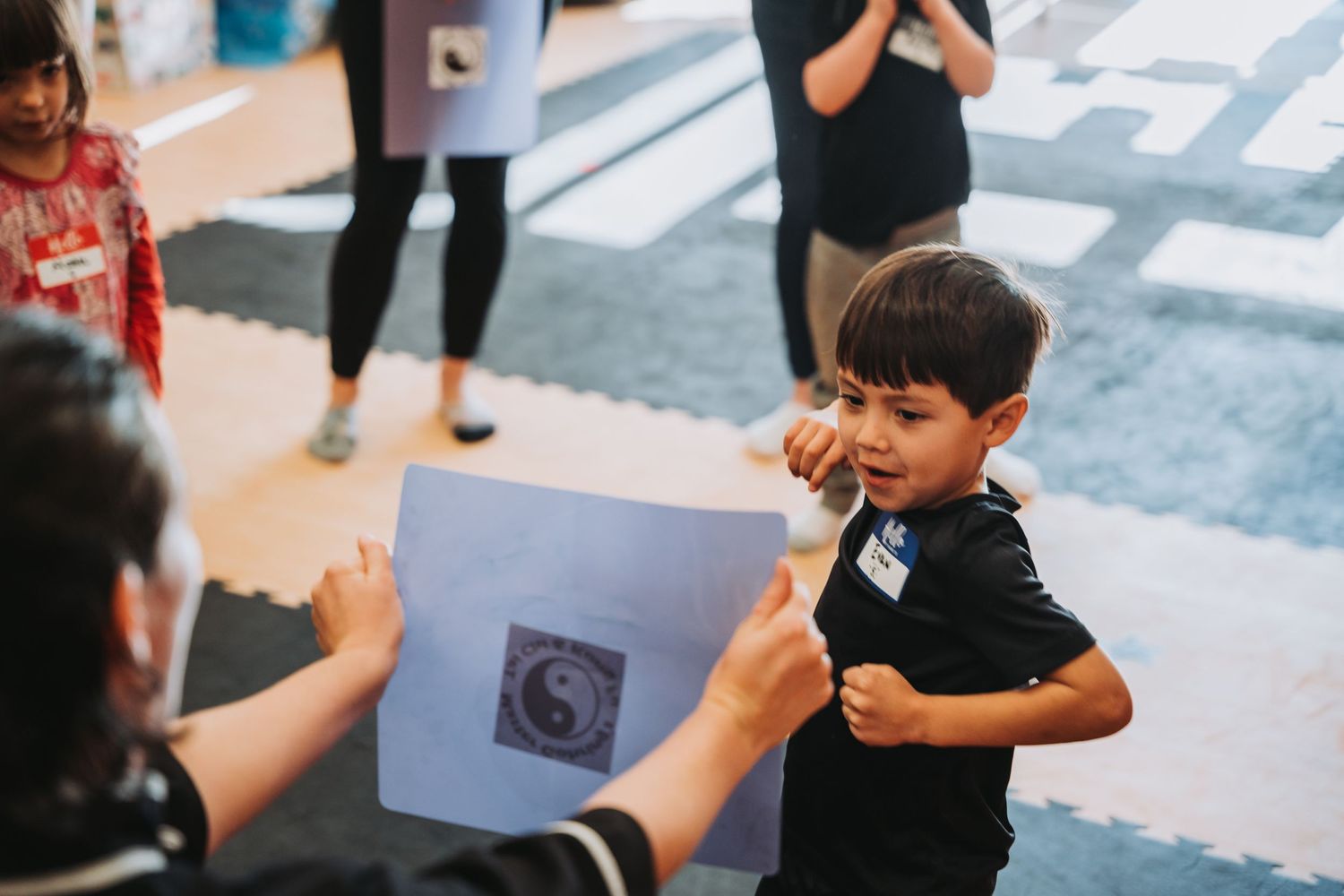 Student receives martial arts instruction while holding a punch pad in training studio.