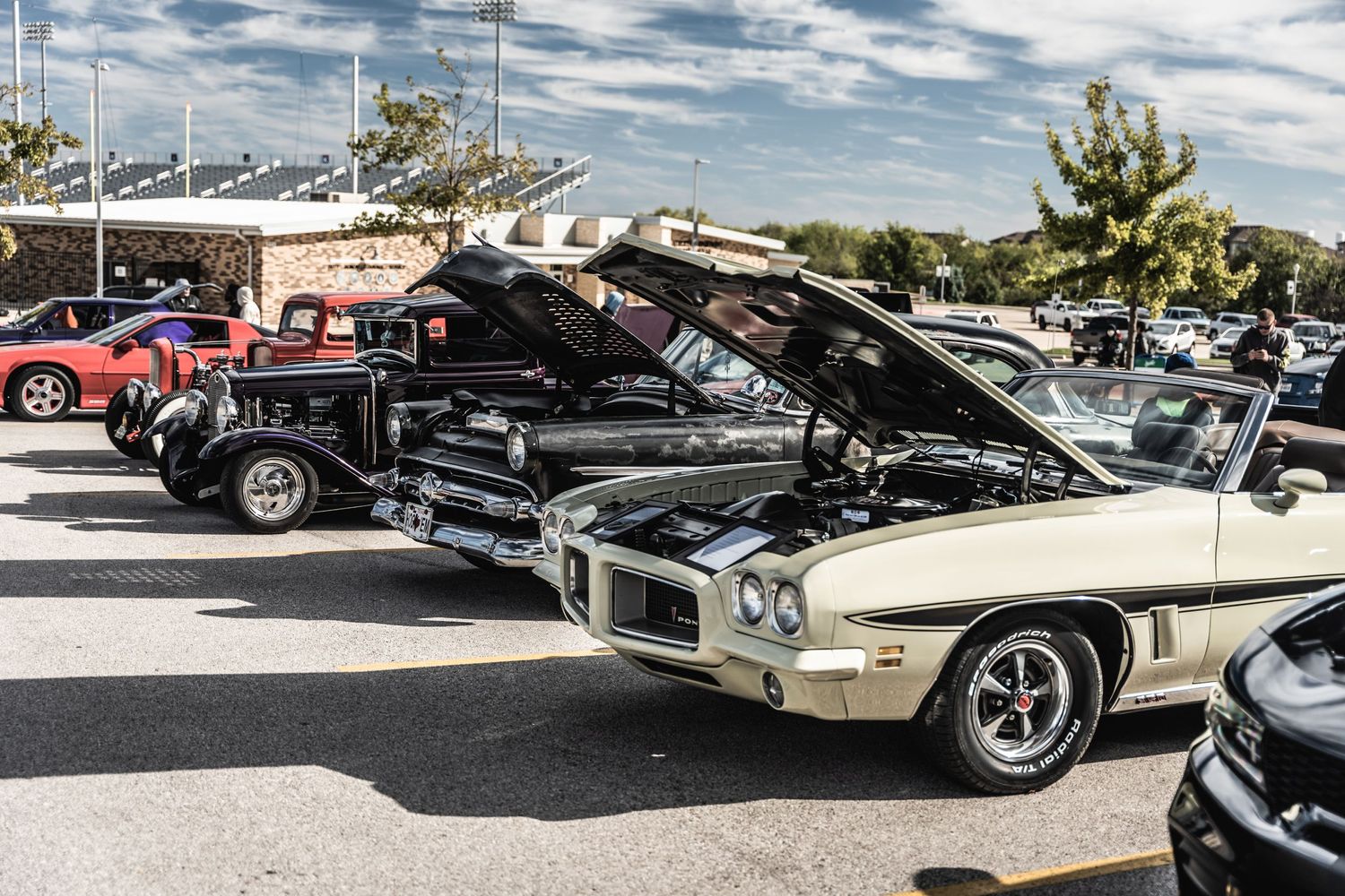 Classic muscle cars with open hoods on display at outdoor car meet.