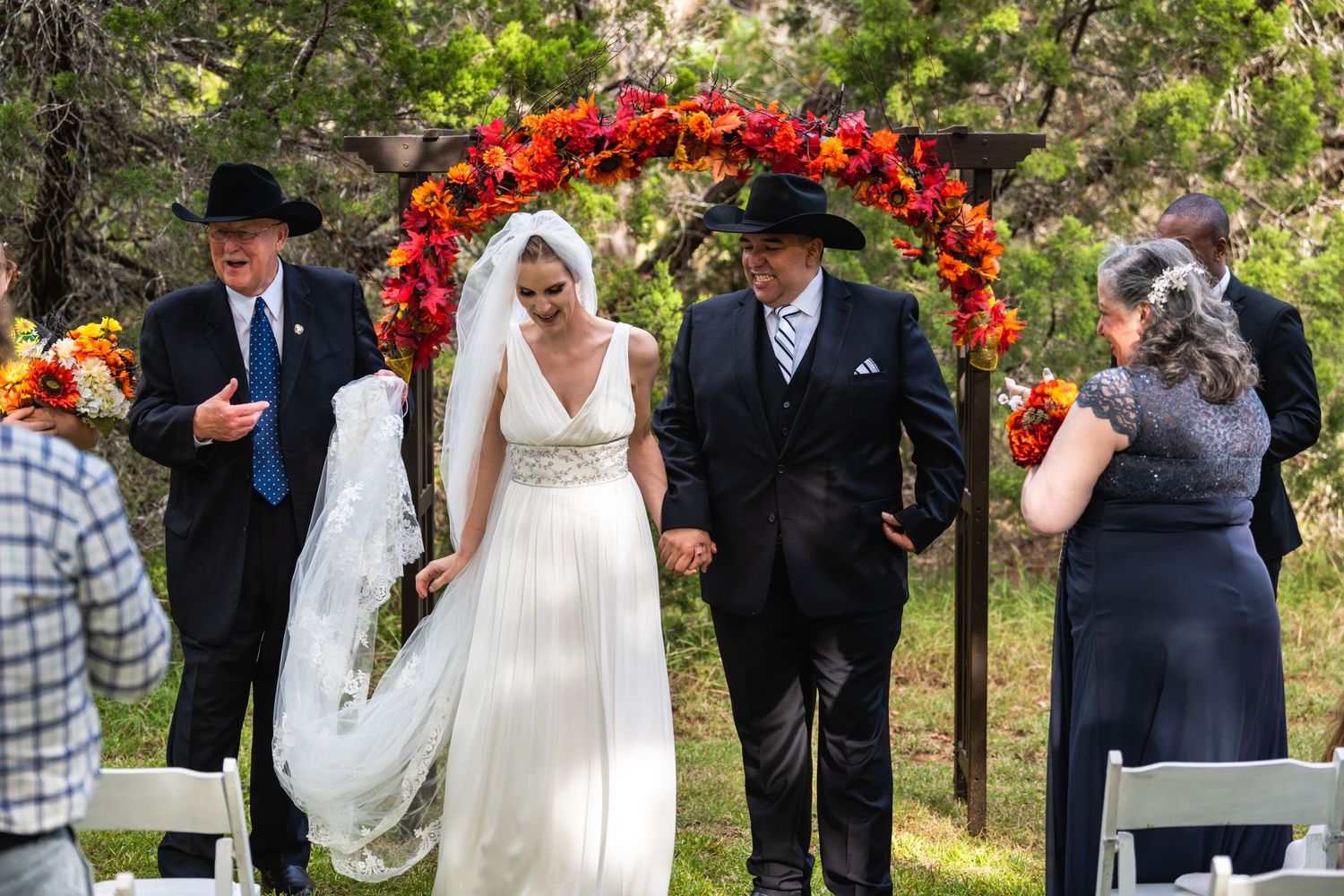 Wedding party exits under a floral arch decorated with vibrant autumn colors.
