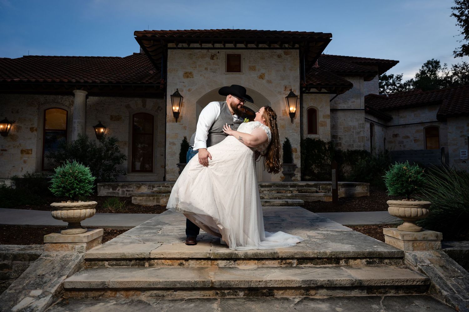 A romantic dip pose on stone steps outside a Mediterranean-style villa at dusk.