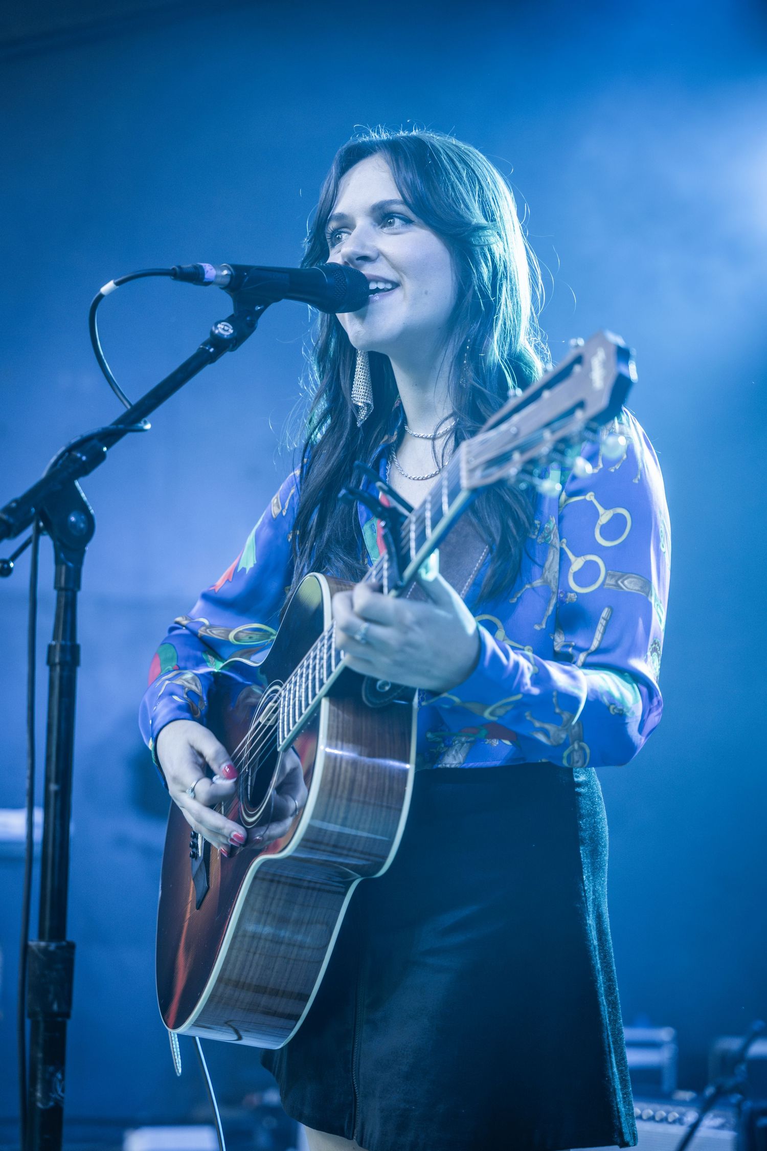Musician singing and playing acoustic guitar during live performance with blue stage lighting.