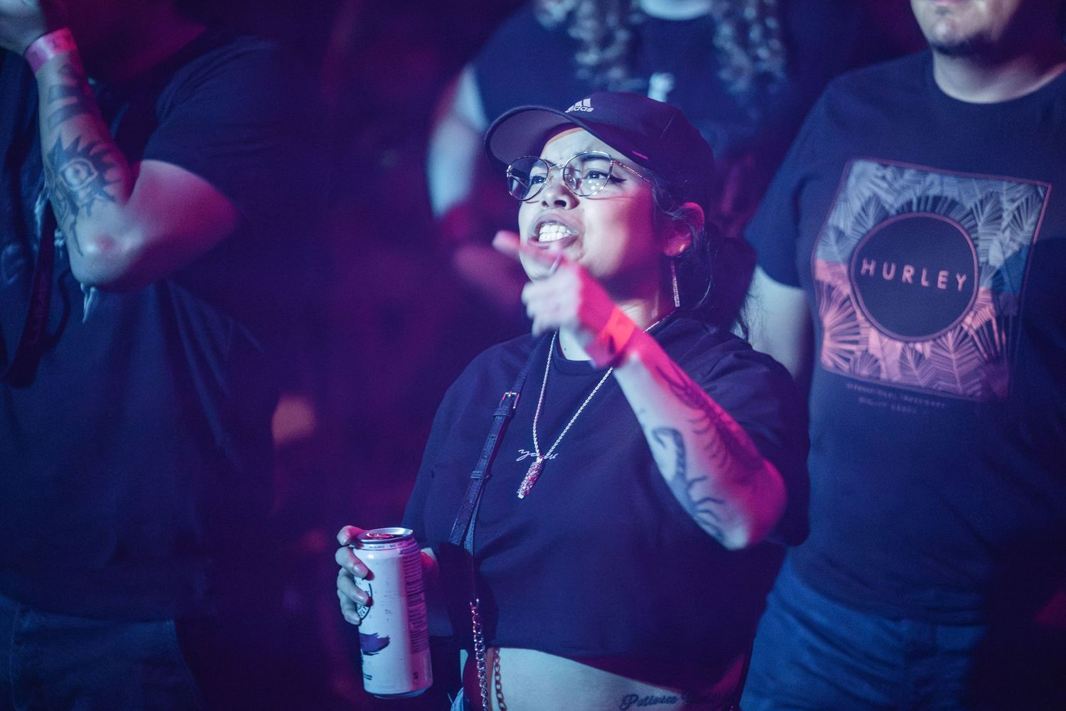 Concert attendee with glasses enjoys live music while holding a drink under neon lights.