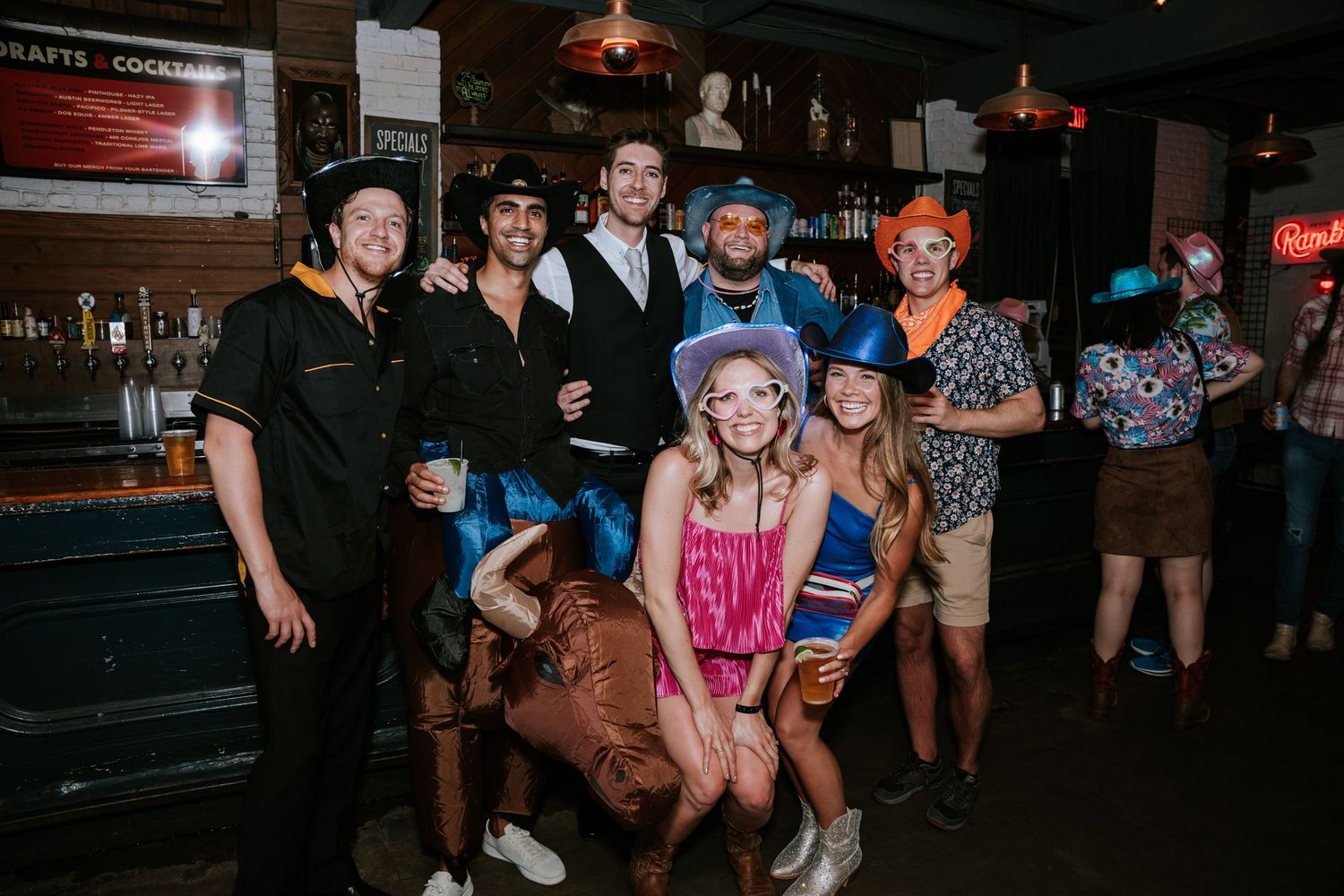 Group of friends gathered at a bar for celebration wearing casual attire and party accessories.