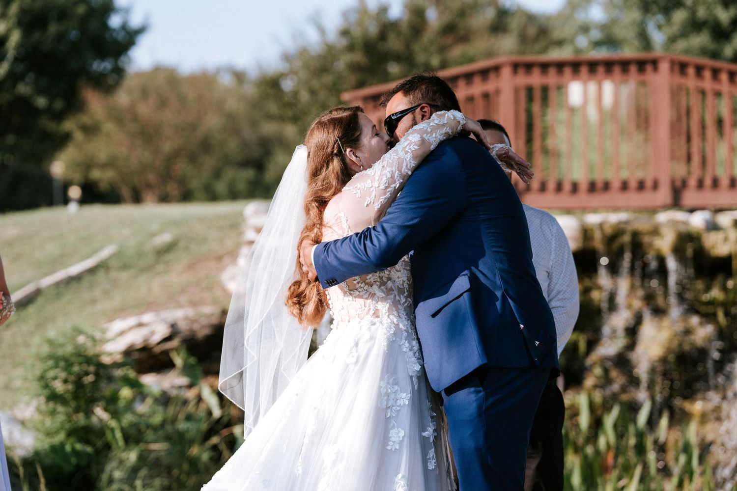 A newlywed couple embraces during their outdoor wedding with a rustic backdrop.