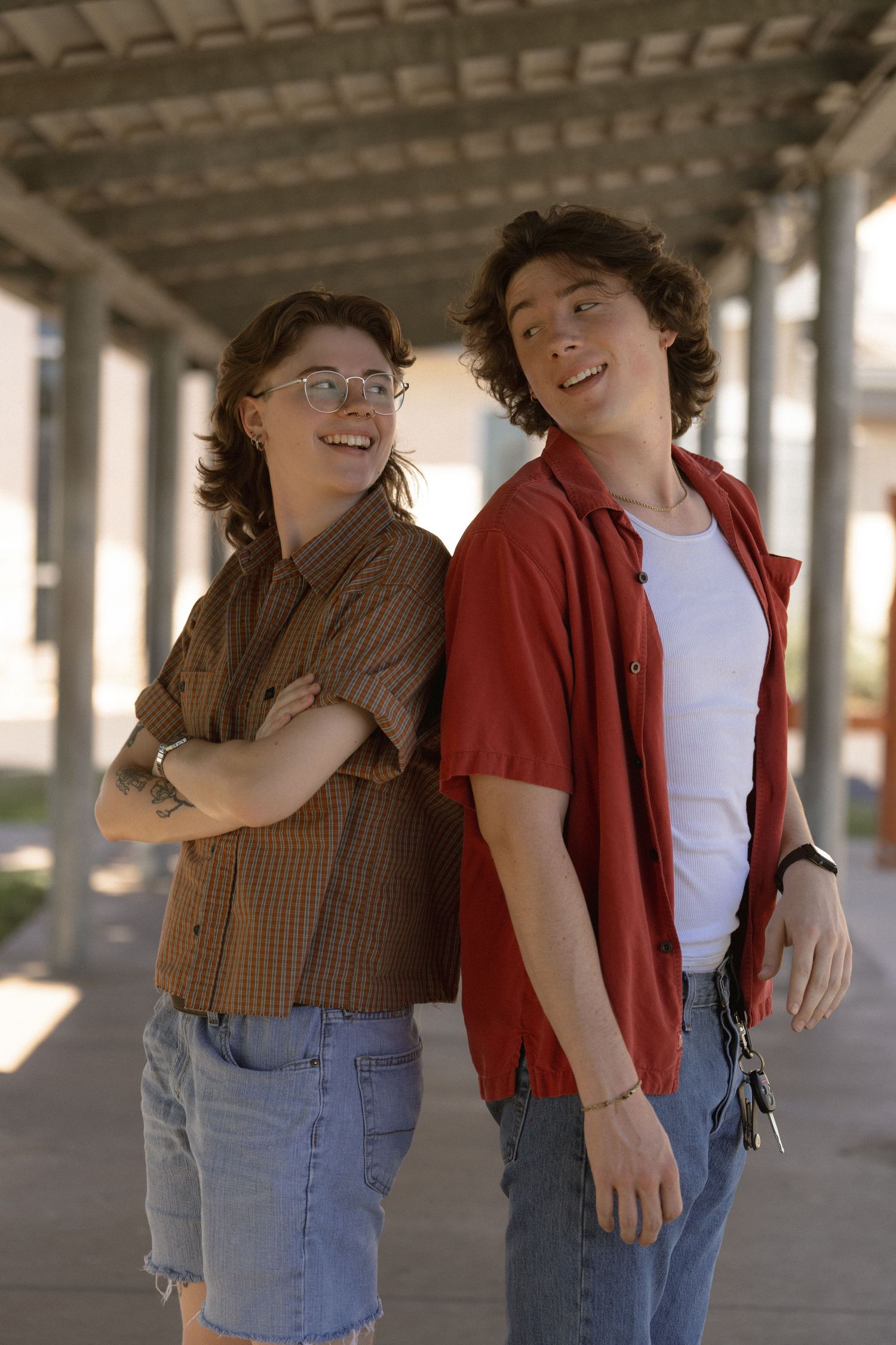 Two friends in casual wear share a laugh while standing under a covered walkway.