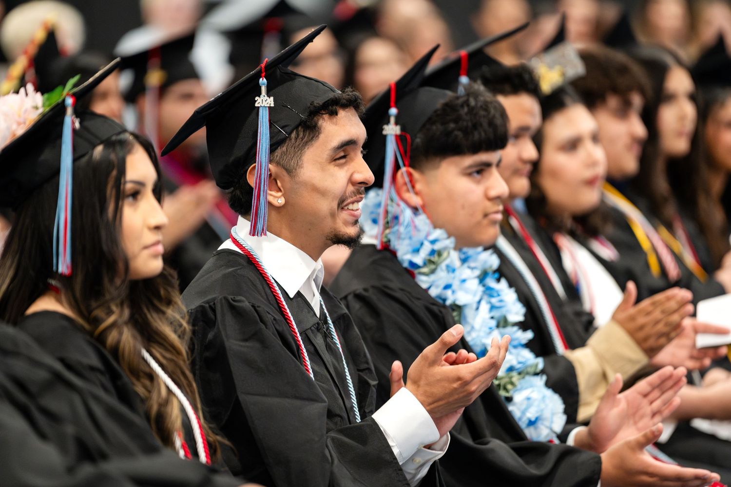 Graduates in caps and gowns applauding during commencement ceremony.