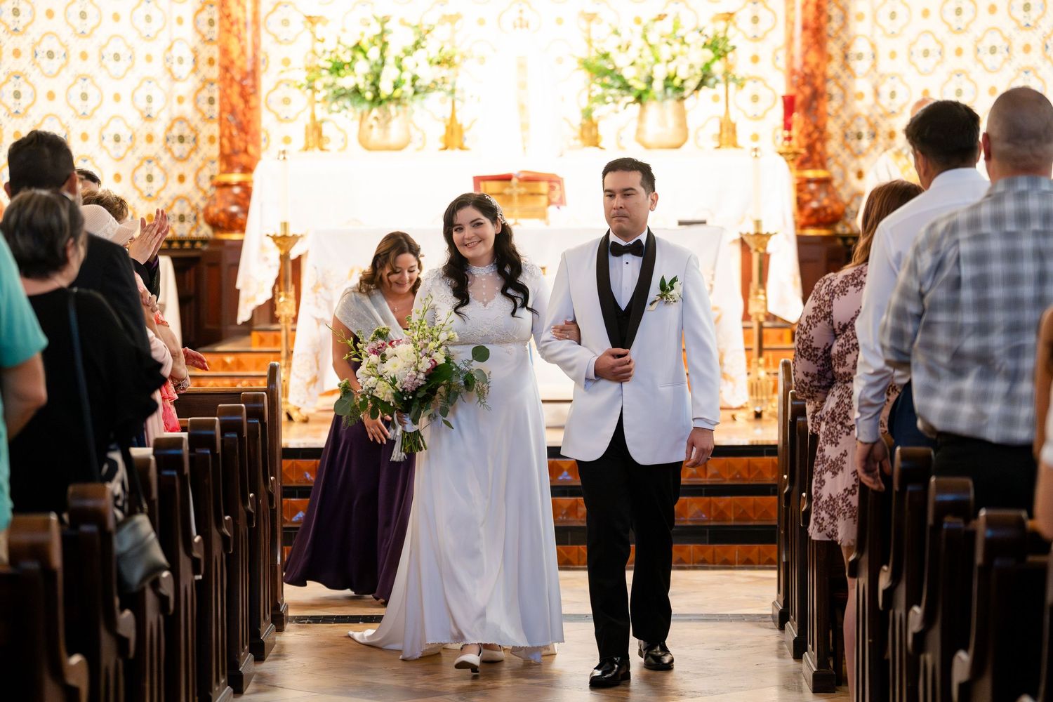 A wedding ceremony in a traditional church sanctuary with stained glass windows and floral decorations.