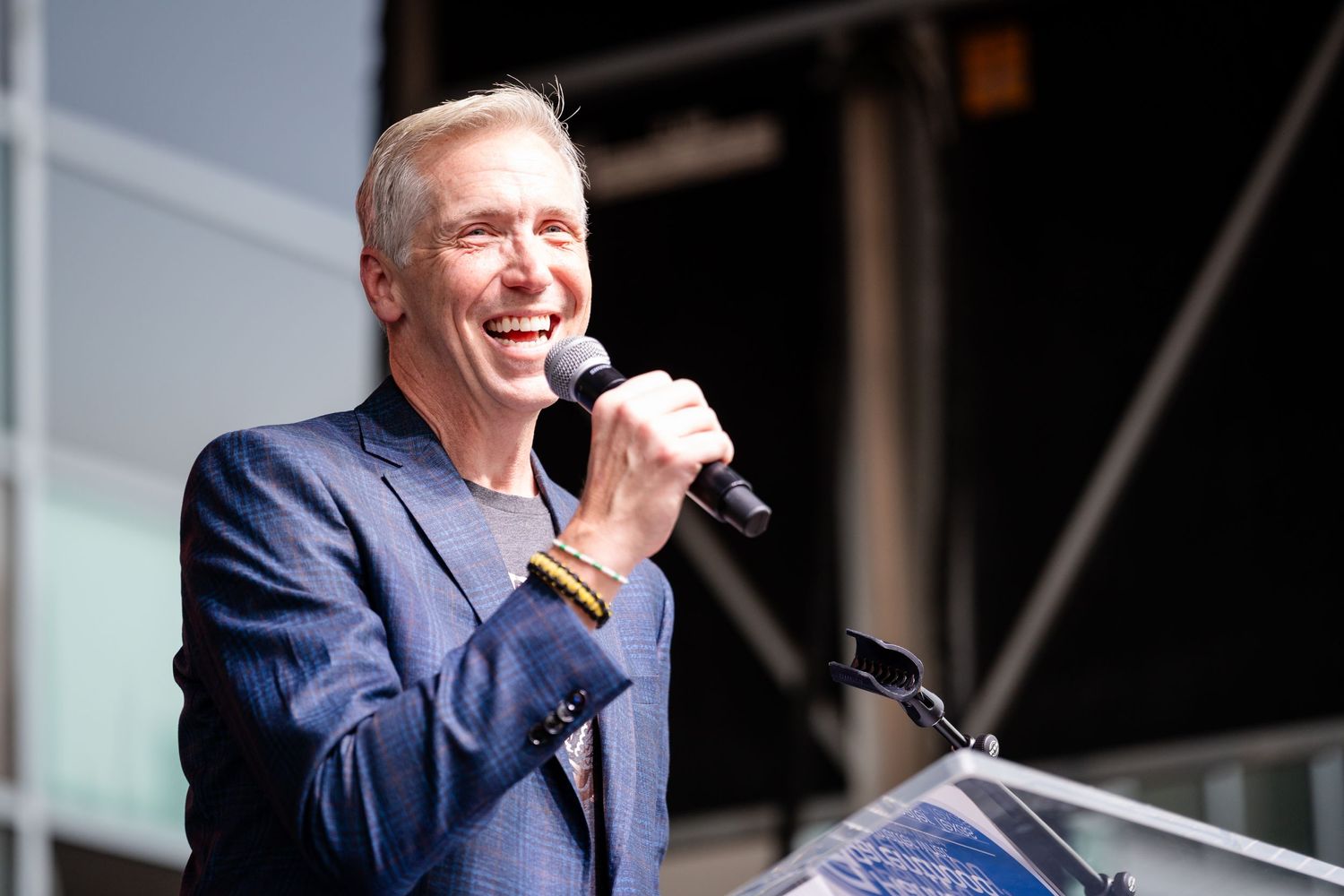 Speaker in navy suit delivers remarks at podium during outdoor event.