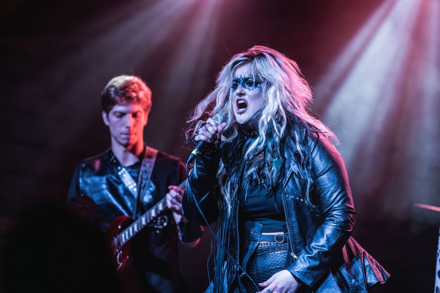 Energetic concert performance with singer in black leather and dramatic lighting effects.