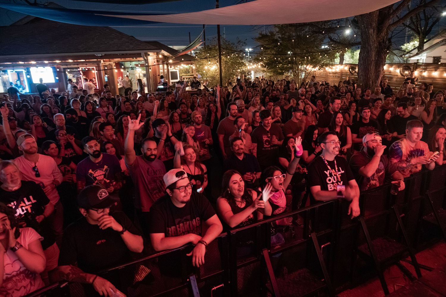 Large crowd of concert-goers enjoying an outdoor music festival at night under string lights.