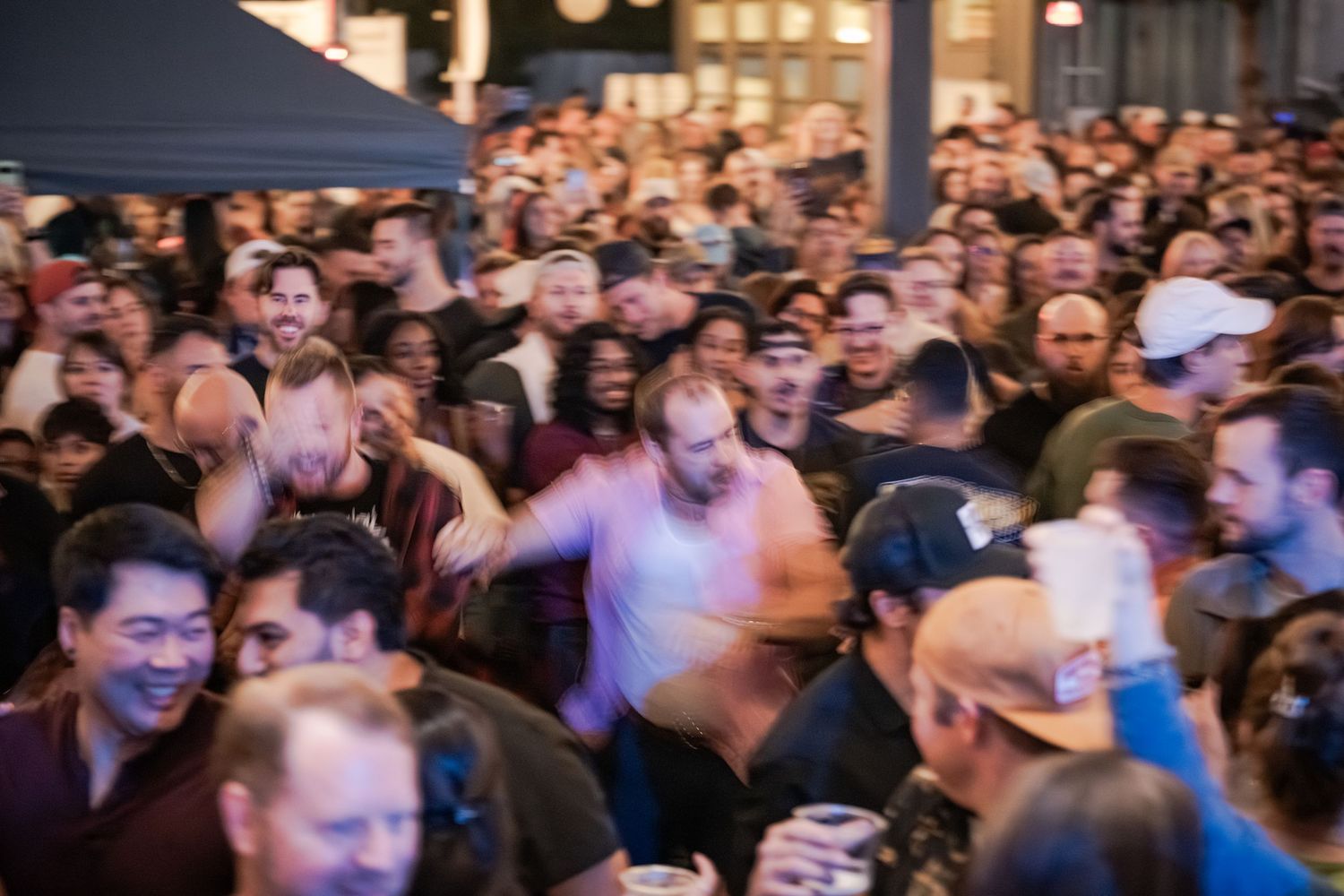 A large crowd of people enjoying a lively outdoor event or concert, with attendees dancing and socializing together.