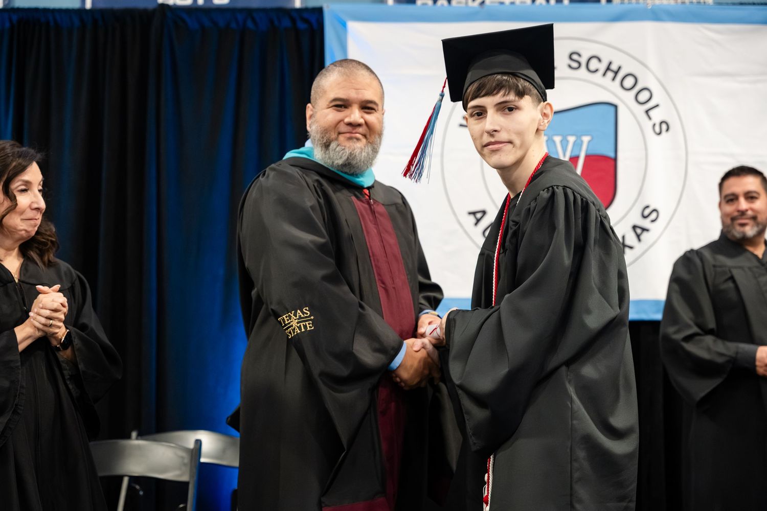 Male graduate in cap and gown shakes hands with school official at Wayside Schools graduation.