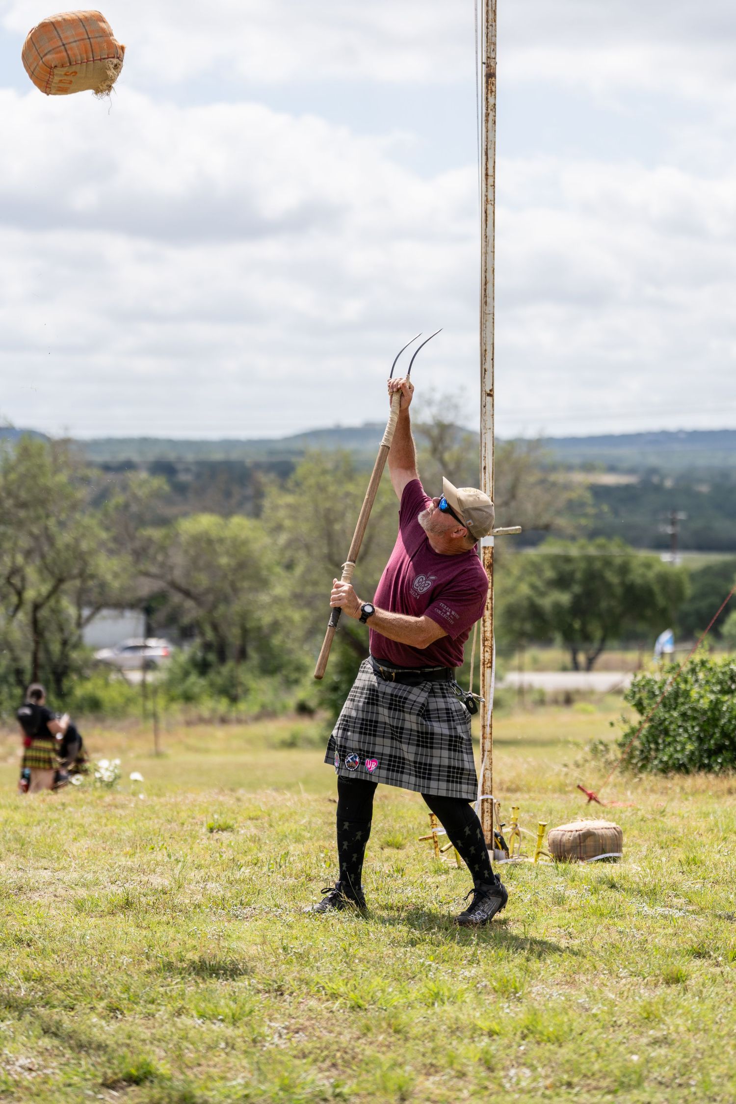 Man in kilt throwing sheaf with pitchfork at Highland Games competition outdoors.