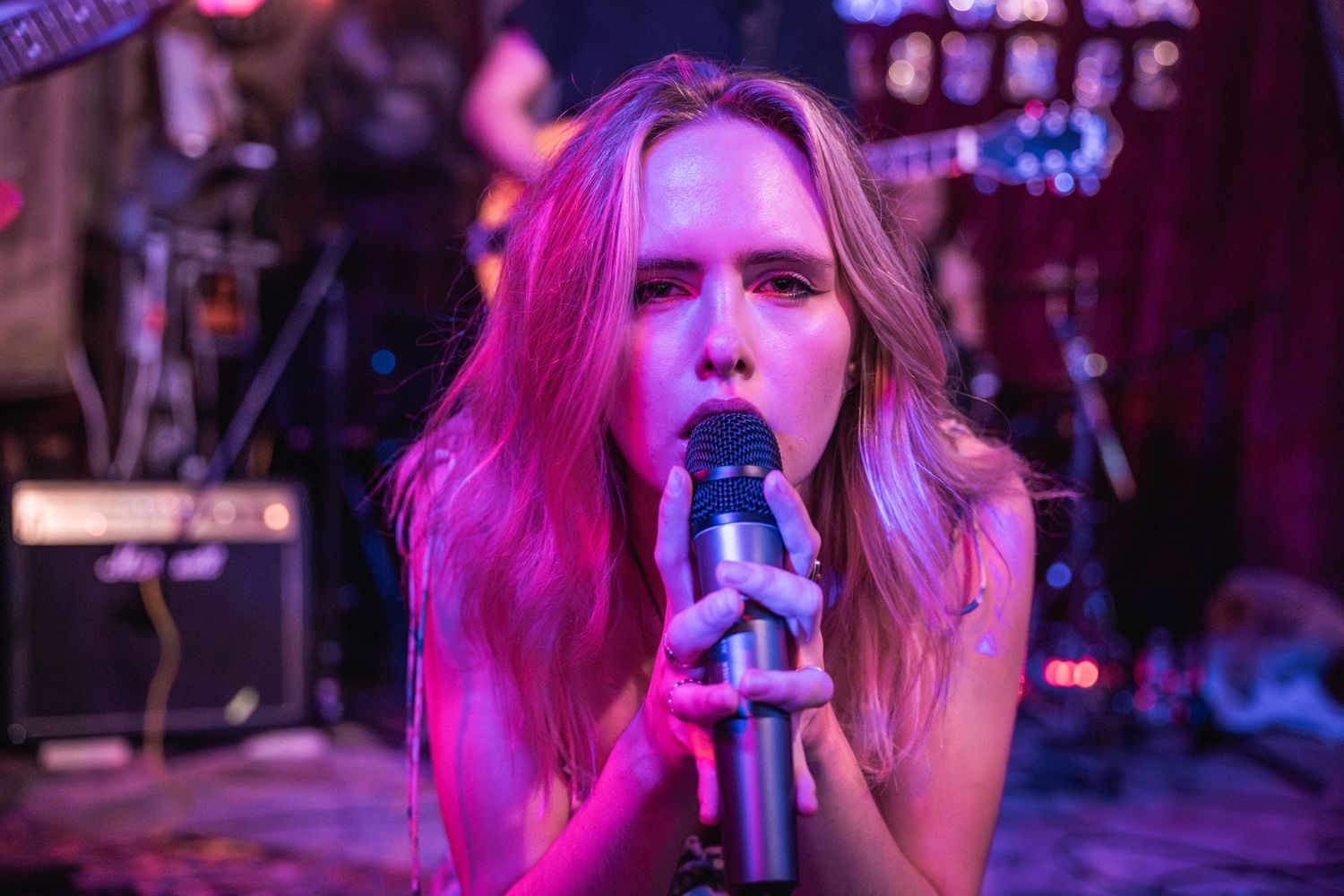 A performer sings passionately on stage under vibrant pink and purple lighting during a live music performance.