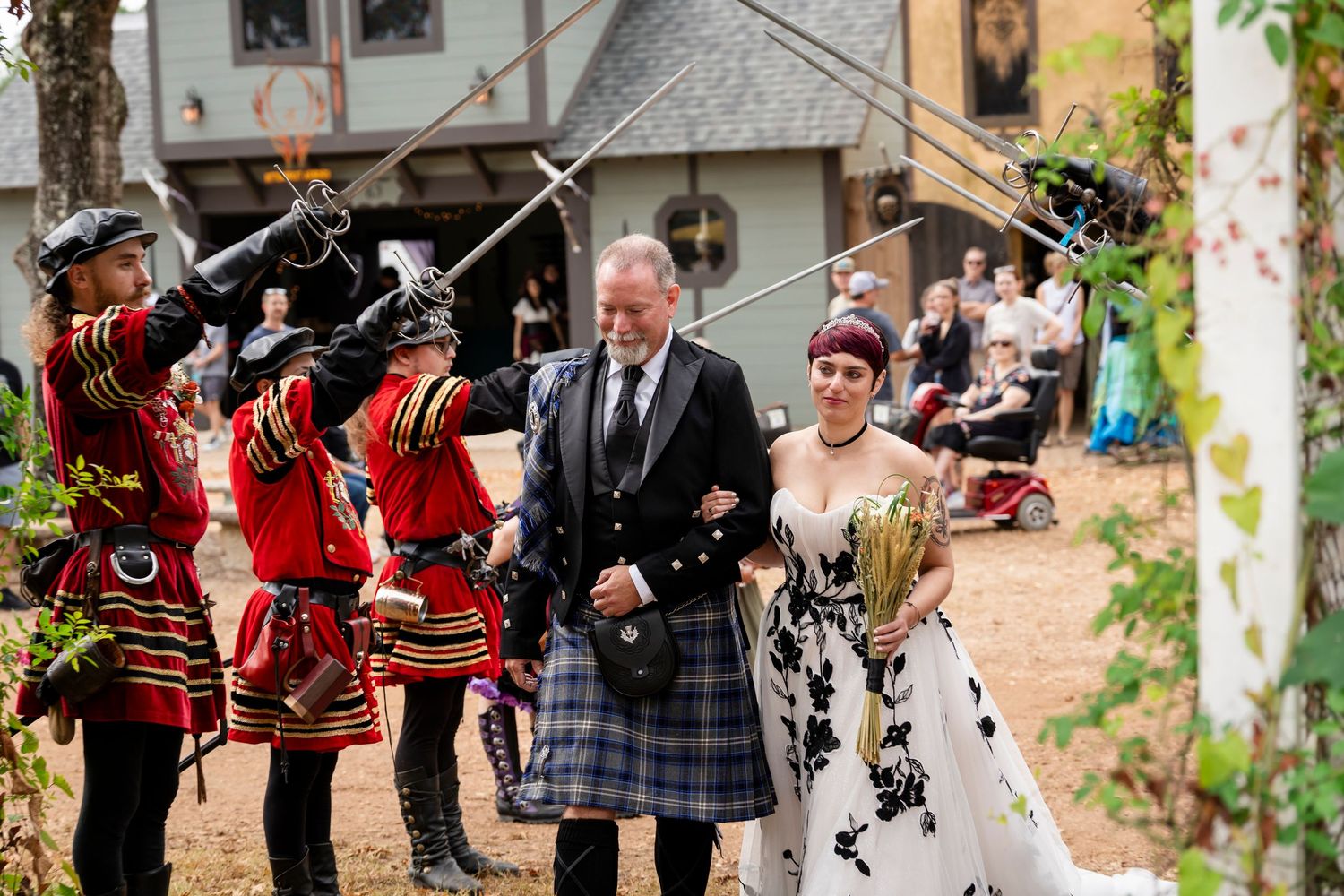 Historical reenactors in red military uniforms perform a ceremonial sword salute at an outdoor Scottish wedding celebration.