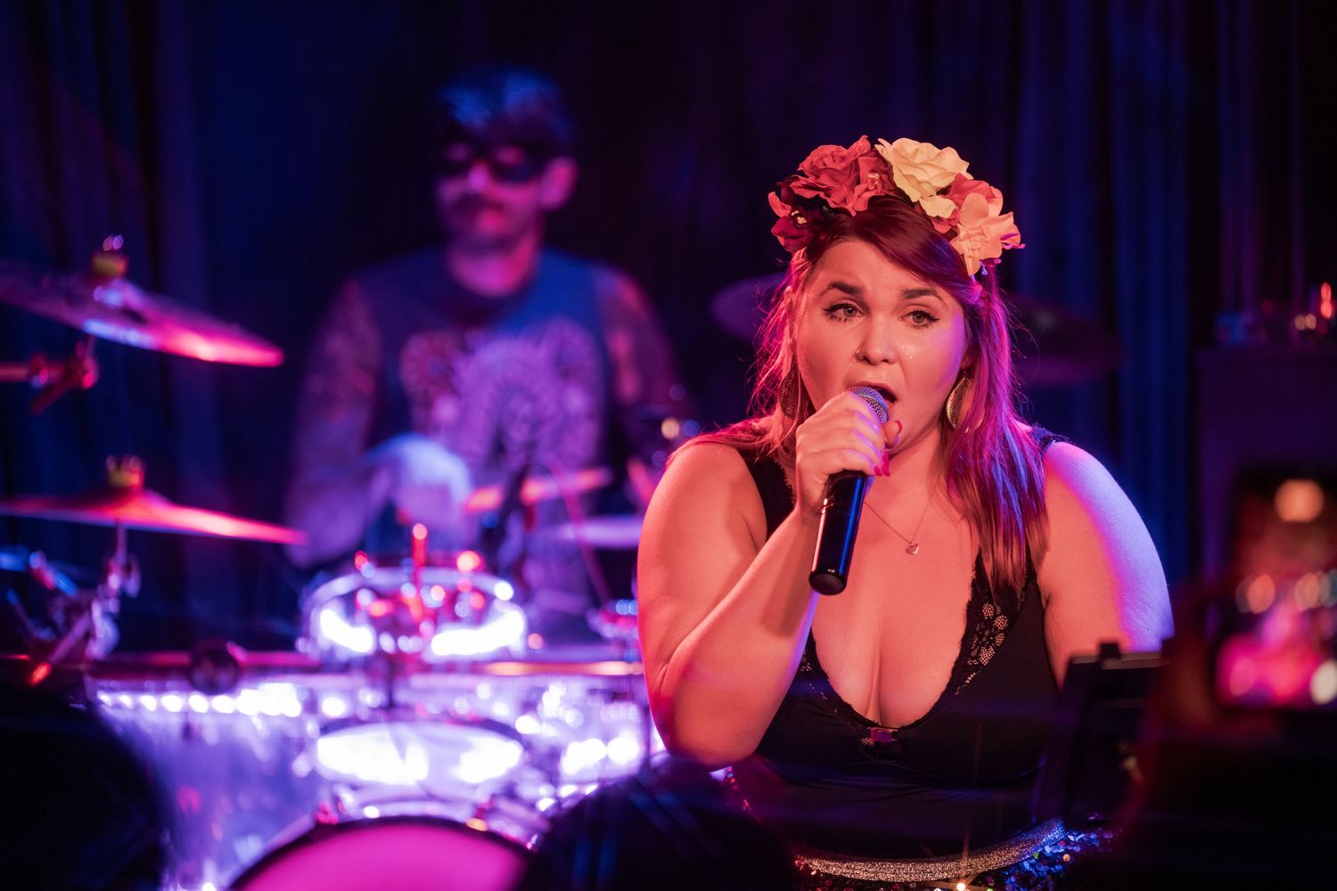 A concert performer sings passionately on stage with dramatic purple and blue lighting in the background.