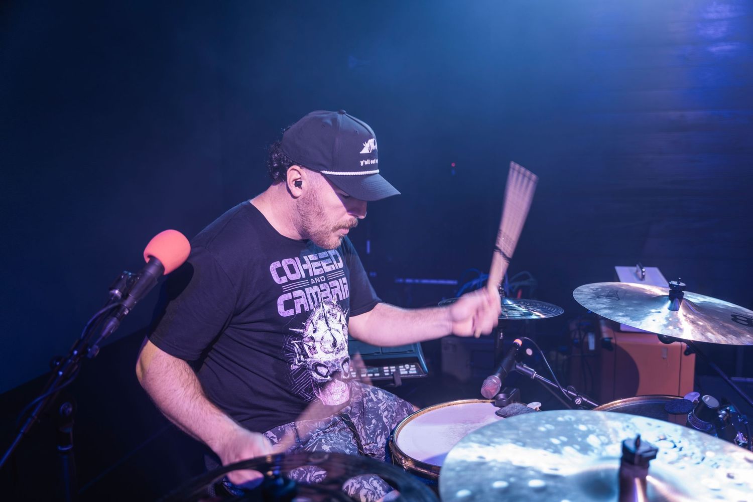 Drummer performing on stage with dramatic blue lighting during a live concert performance.