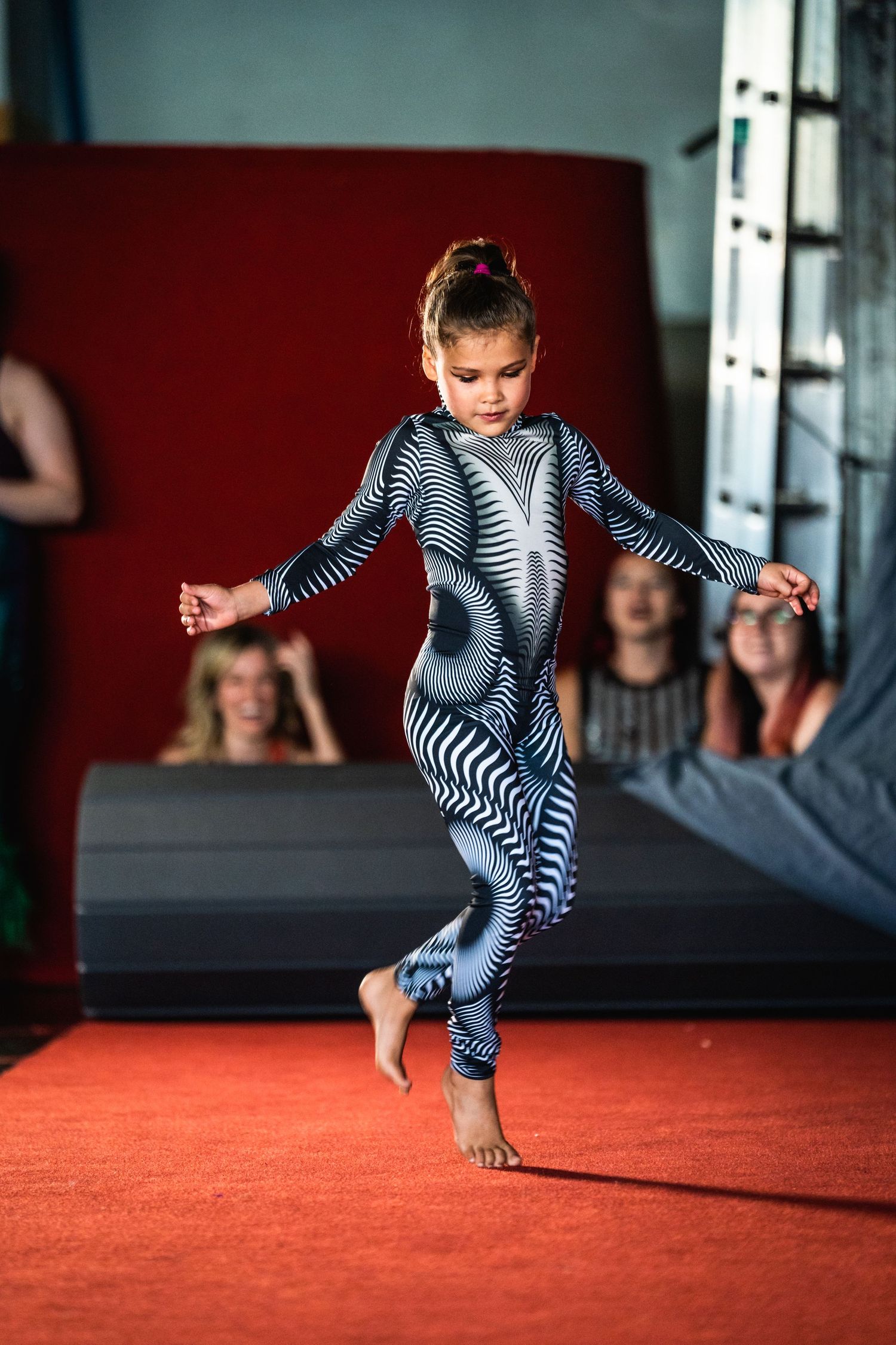Child in striped bodysuit performs gymnastic moves on red mat in sequence of action shots.