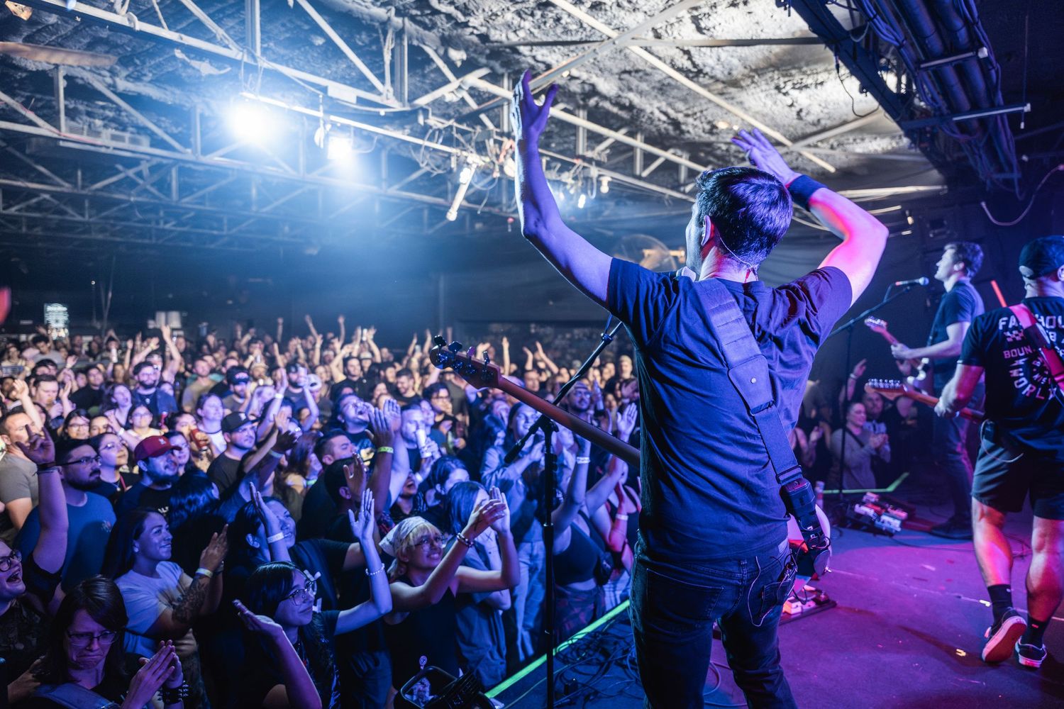 A crowd of enthusiastic concert-goers enjoy a live performance with dramatic blue and purple stage lighting.