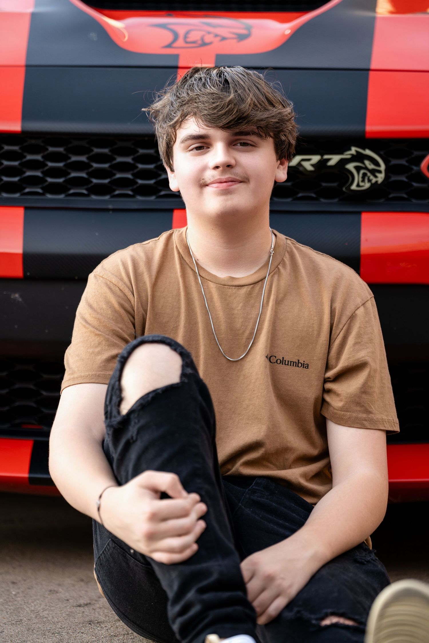 A casual portrait against the hood of a red Dodge Charger with custom black graphics.