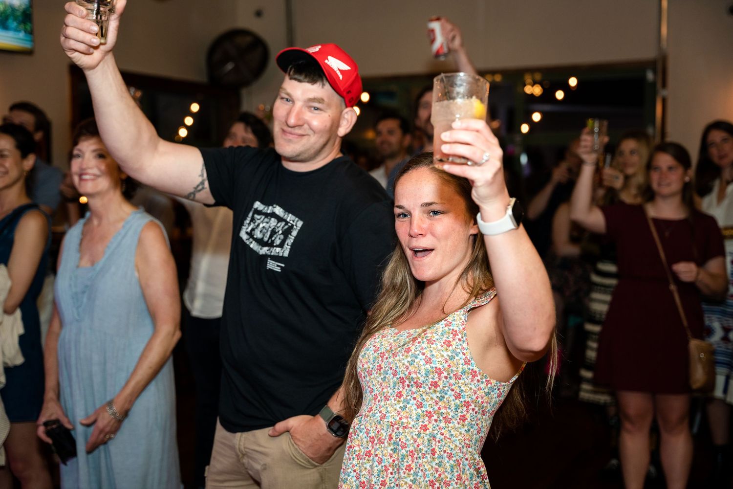 Party guests raising drinks enthusiastically during a lively indoor celebration event.