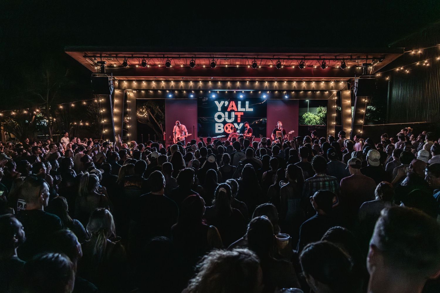 Large outdoor concert venue at night with illuminated stage and crowd silhouettes.