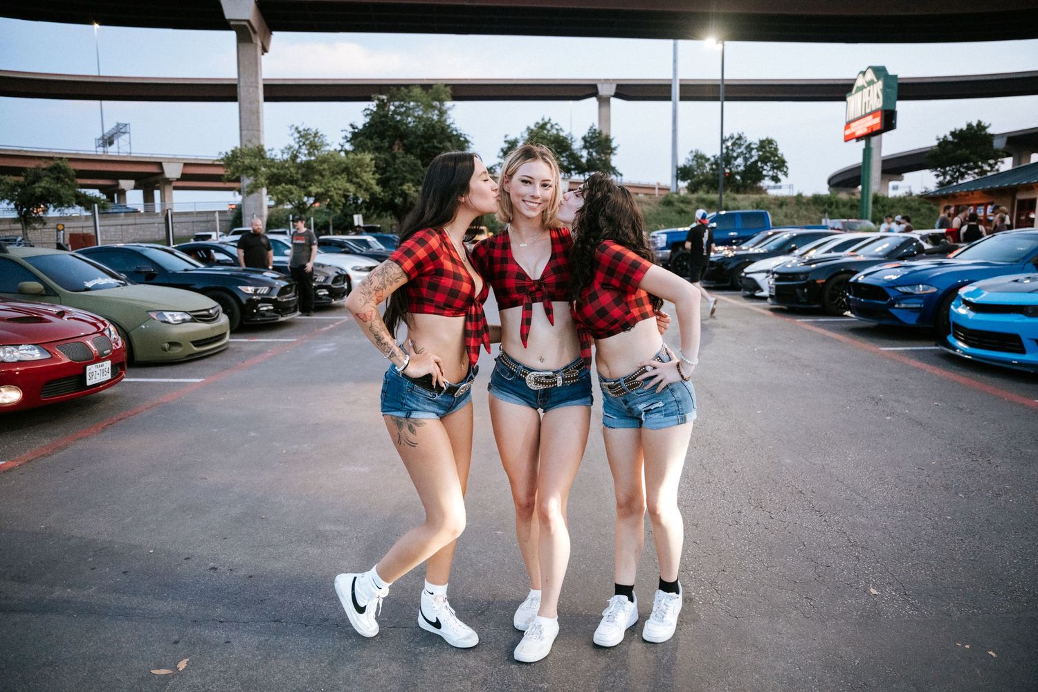 Friends posing together at a car meet in matching outfits.