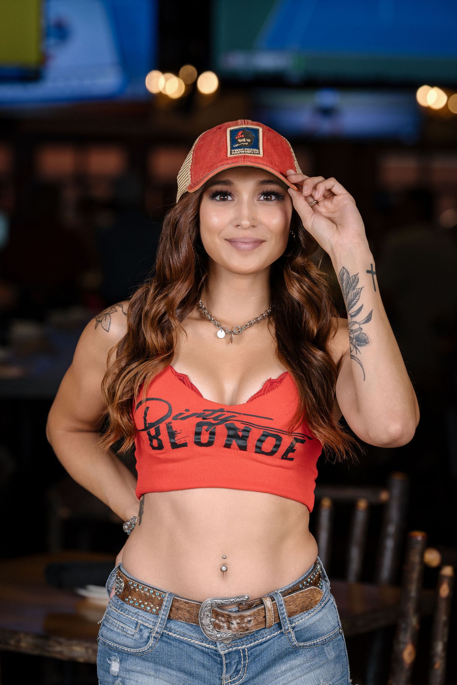 Person in red crop top and baseball cap poses in casual restaurant setting.