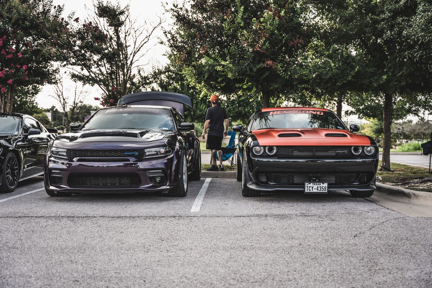 Purple Dodge Challenger Hellcat parked next to an orange muscle car at a car meet.