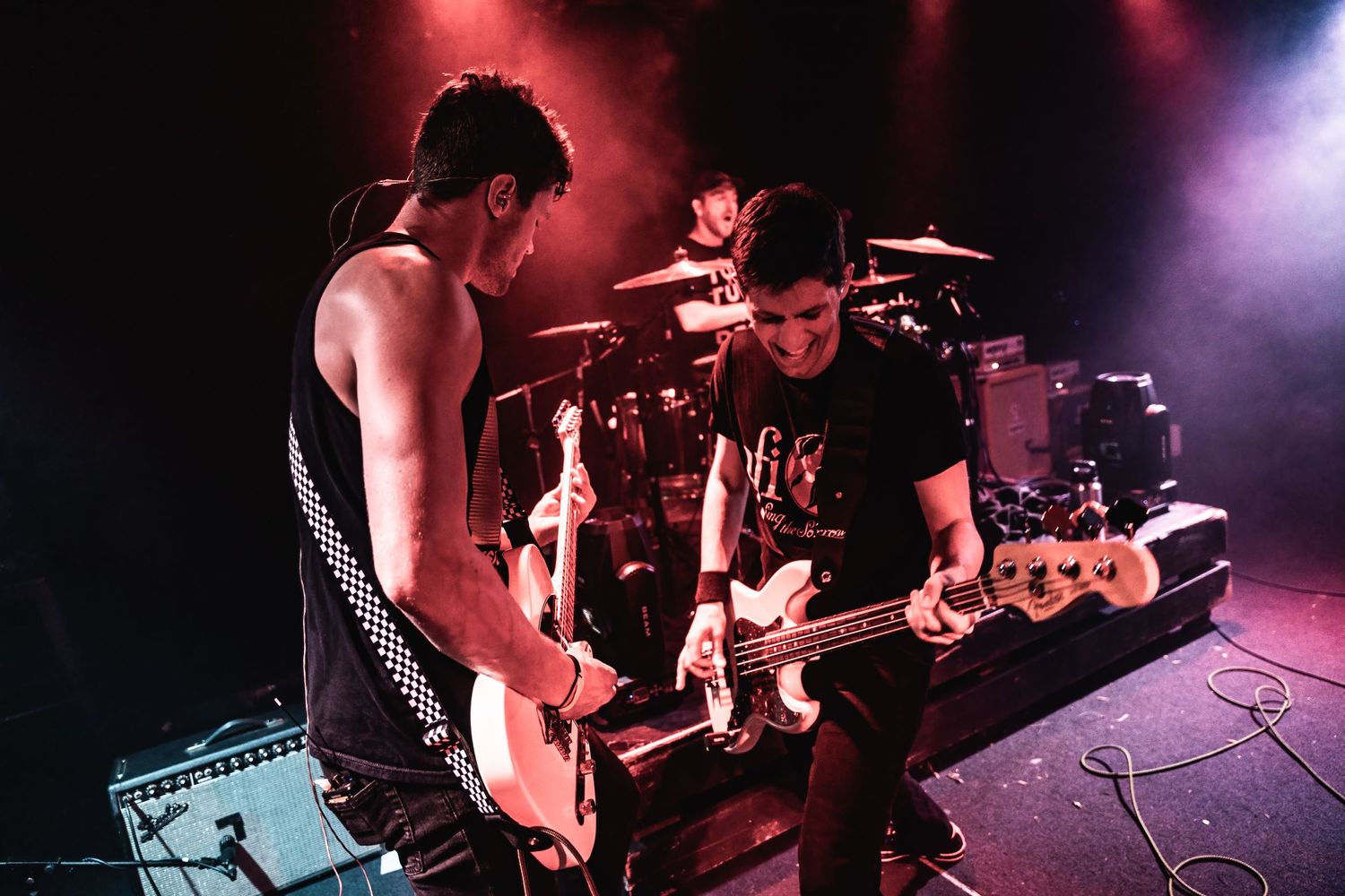 Two musicians performing together on stage with red atmospheric lighting and smoke effects.