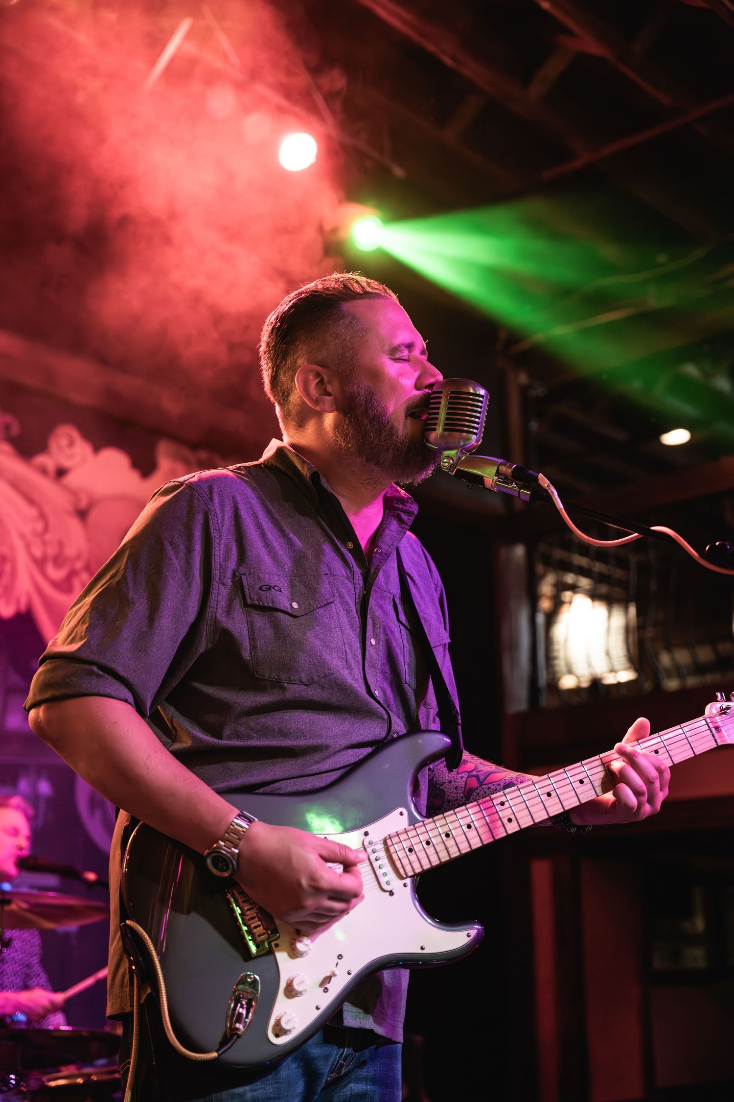 Performer plays white electric guitar under vibrant red and green stage lights.