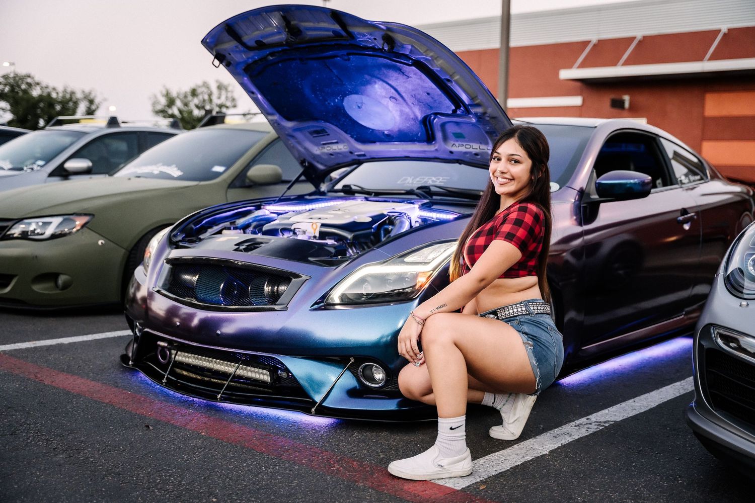 Modified blue car with open hood on display in parking lot during car meet.