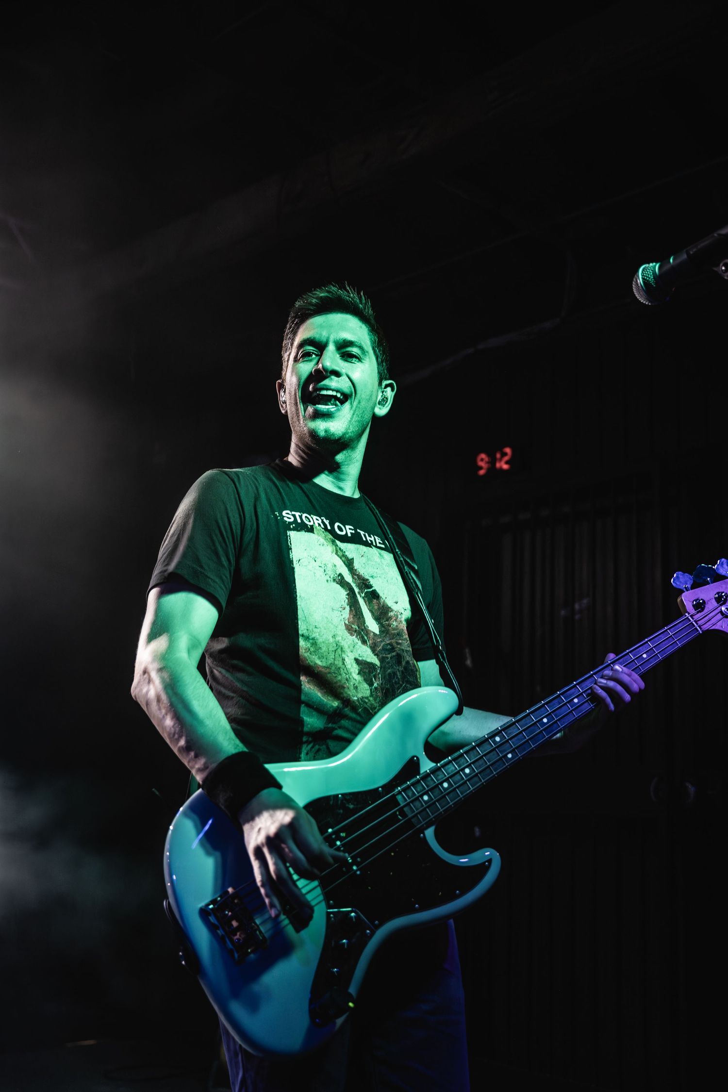 Bass player performs energetically on stage with dramatic green lighting effects.