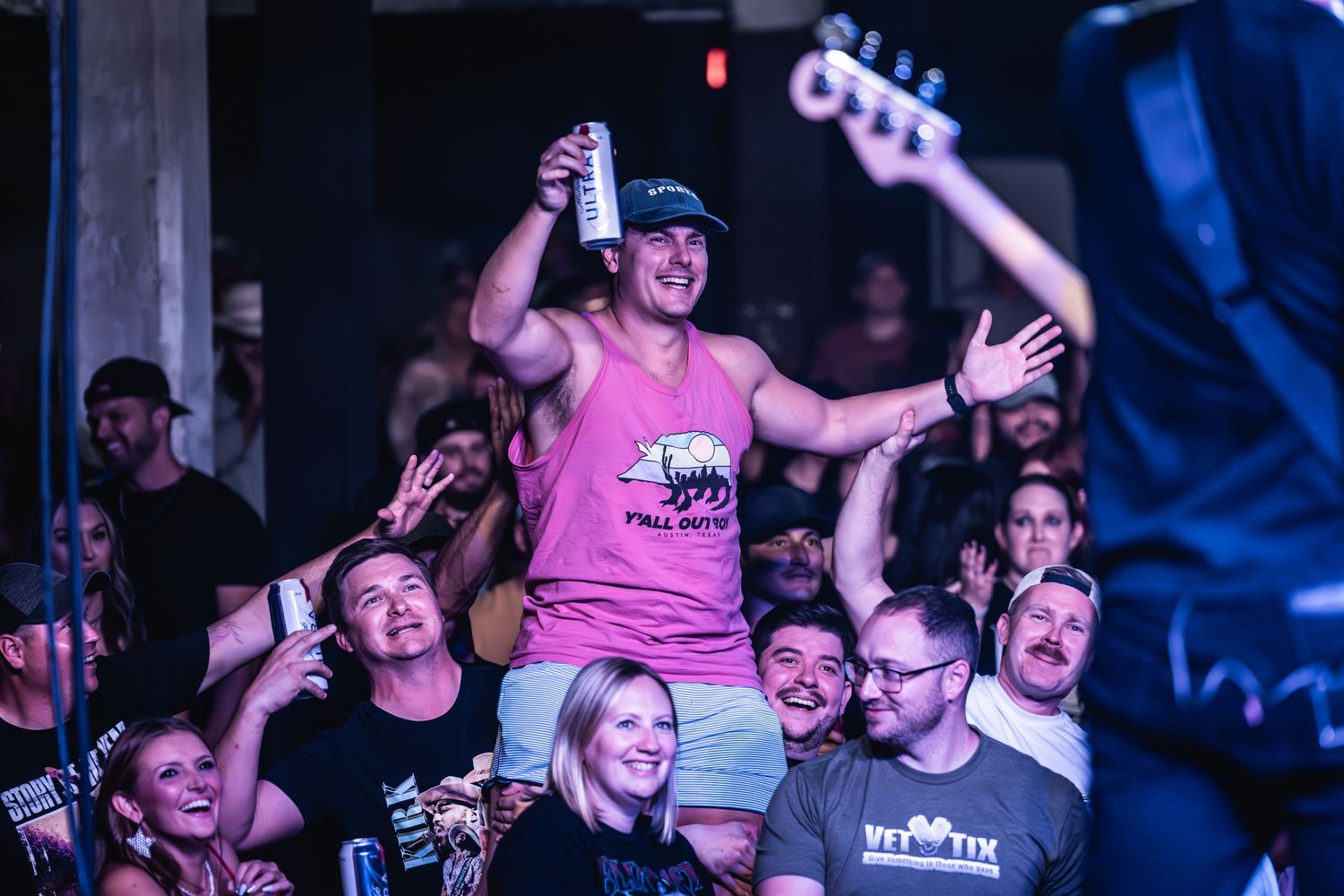 Concertgoer in pink shirt crowd surfs above an energetic audience.