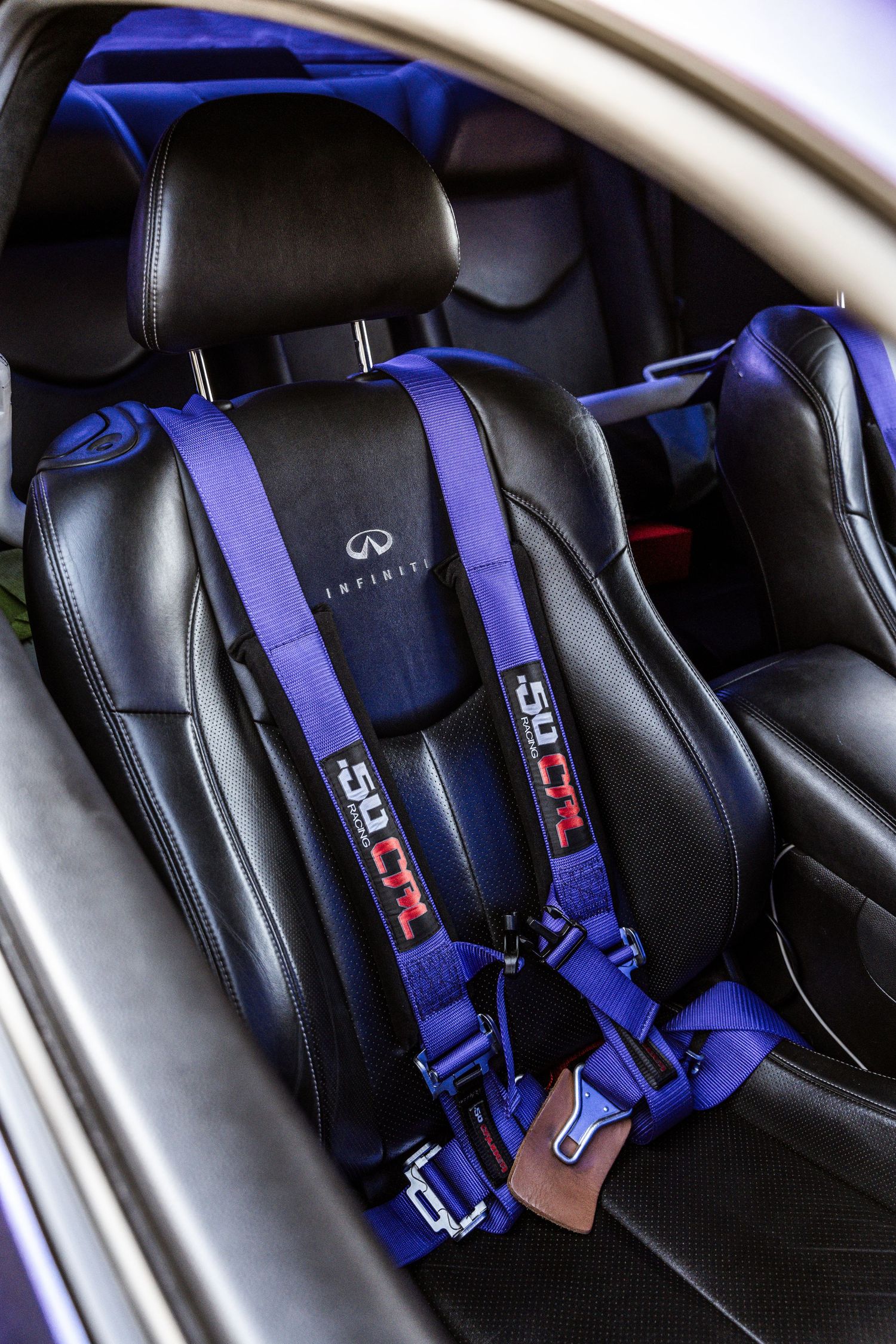 Black leather car interior with blue racing harness seatbelts and Infiniti branded seats.