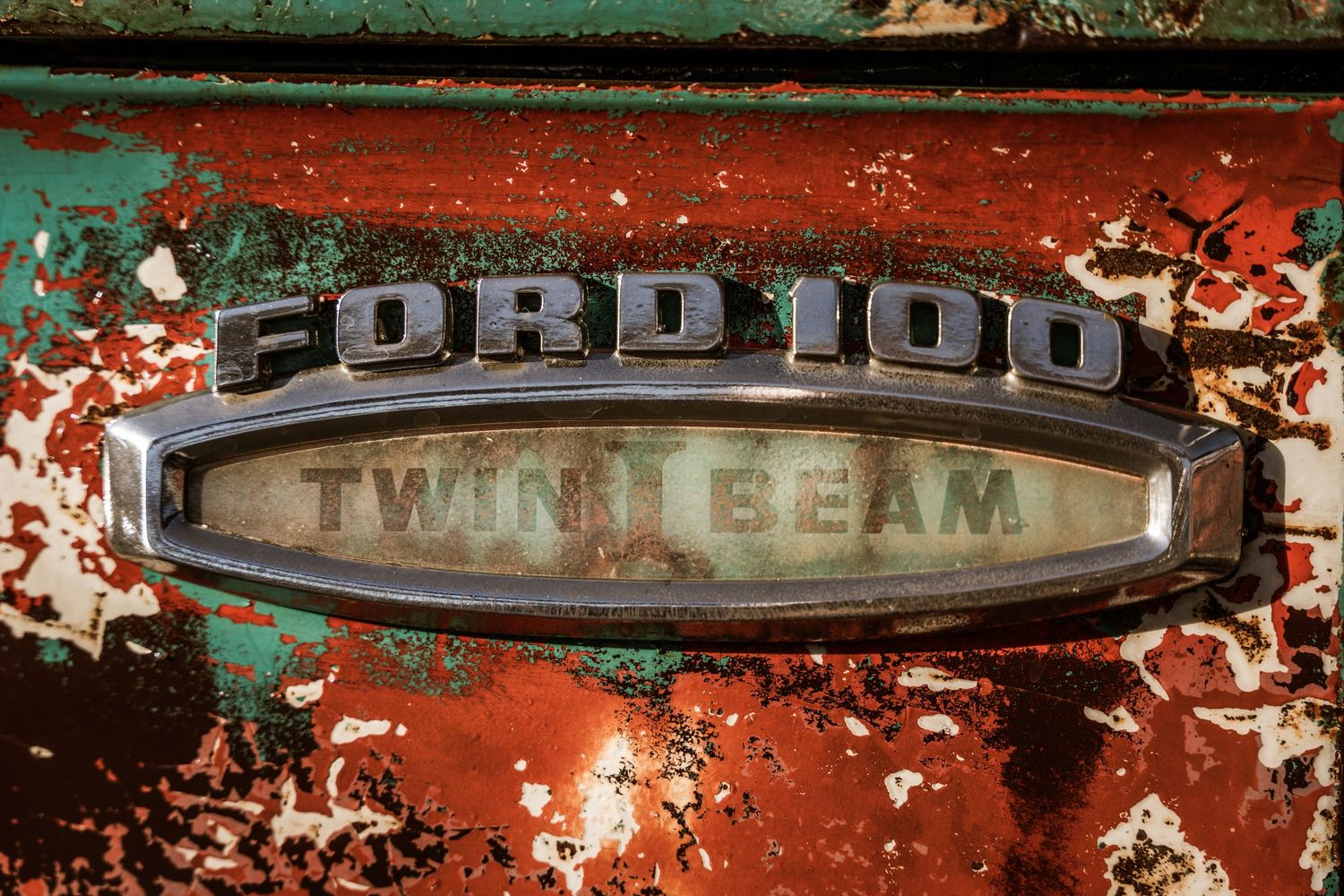 Vintage Ford 100 Twin I-Beam badge with peeling paint and patina.