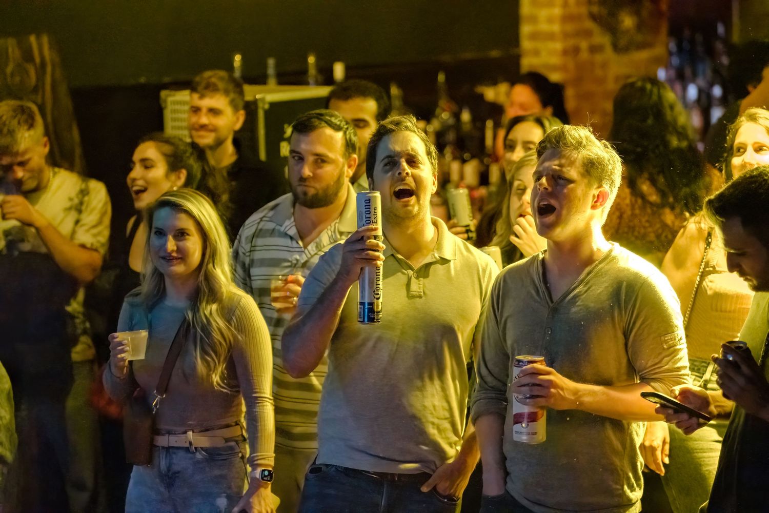 Concert attendees holding drinks while watching performance under warm lighting.