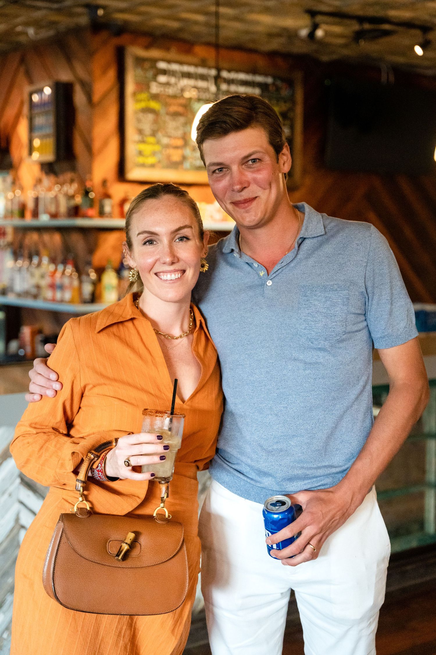 Couple enjoying drinks at rustic bar with exposed brick wall and warm lighting.