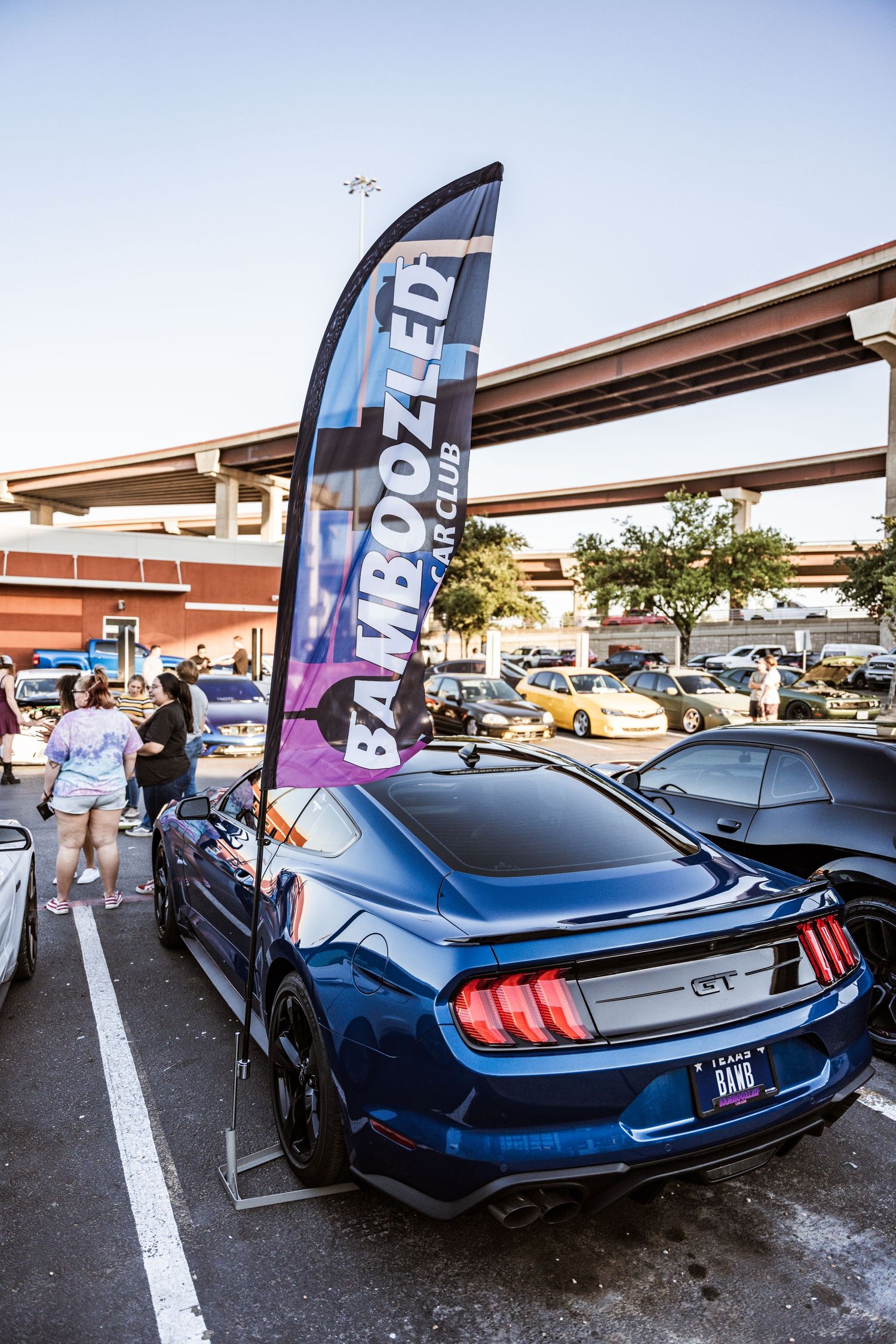 Blue Ford Mustang GT with custom modifications parked under promotional banner.