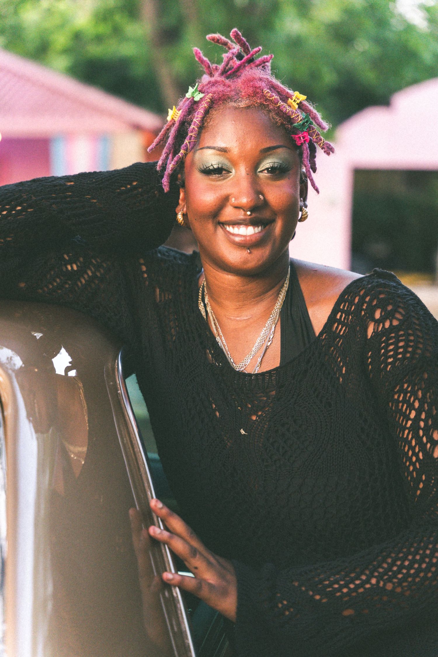 Woman wearing a black crochet top and pink braids poses outdoors with a bright smile.