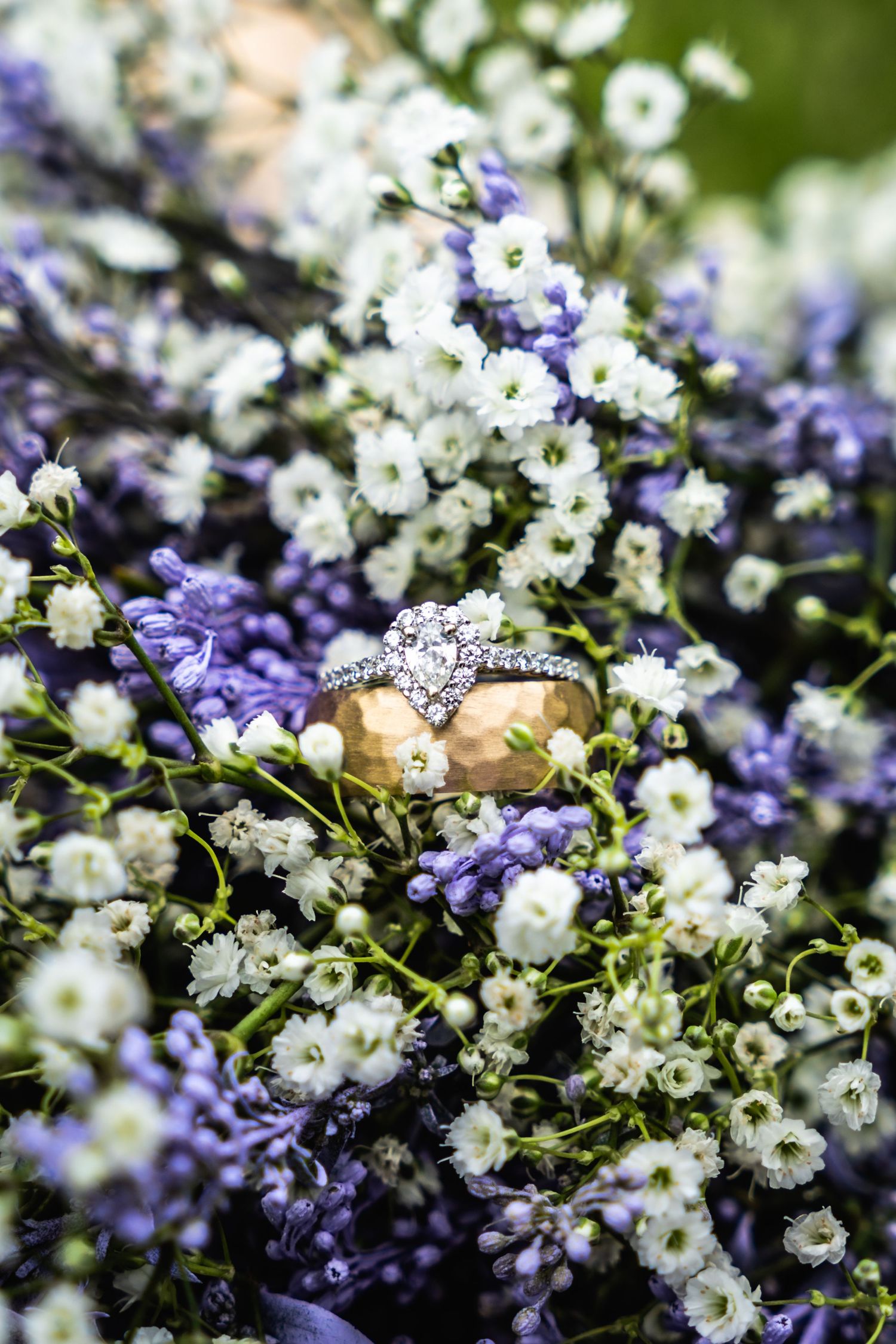Wedding rings nestled among white and purple flowers in a delicate floral arrangement.