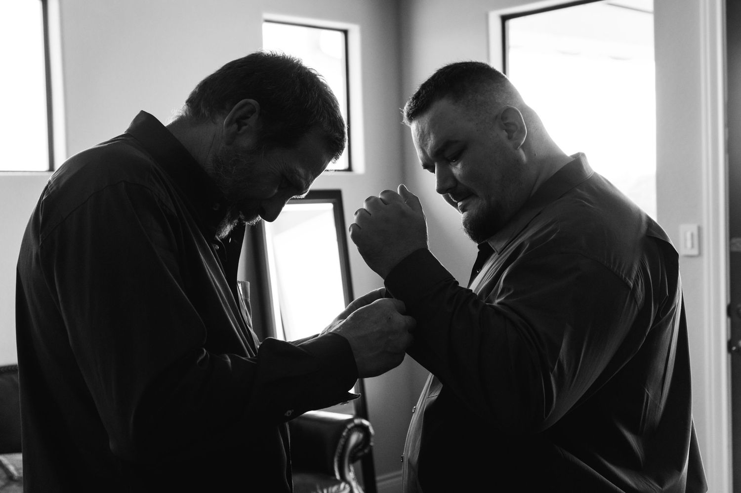 Two figures bow their heads in prayer together in black and white.